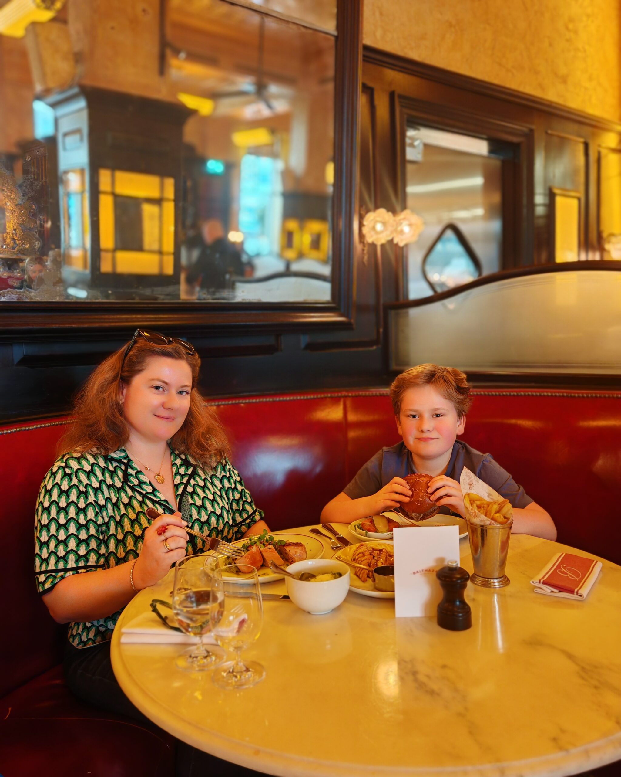 A white woman with her son eating in a brasserie restaurant in London, Covent Garden. The table is gold and he is eating a burger. A white woman with her son eating in a brasserie restaurant in London, Covent Garden. The table is gold and he is eating a burger.