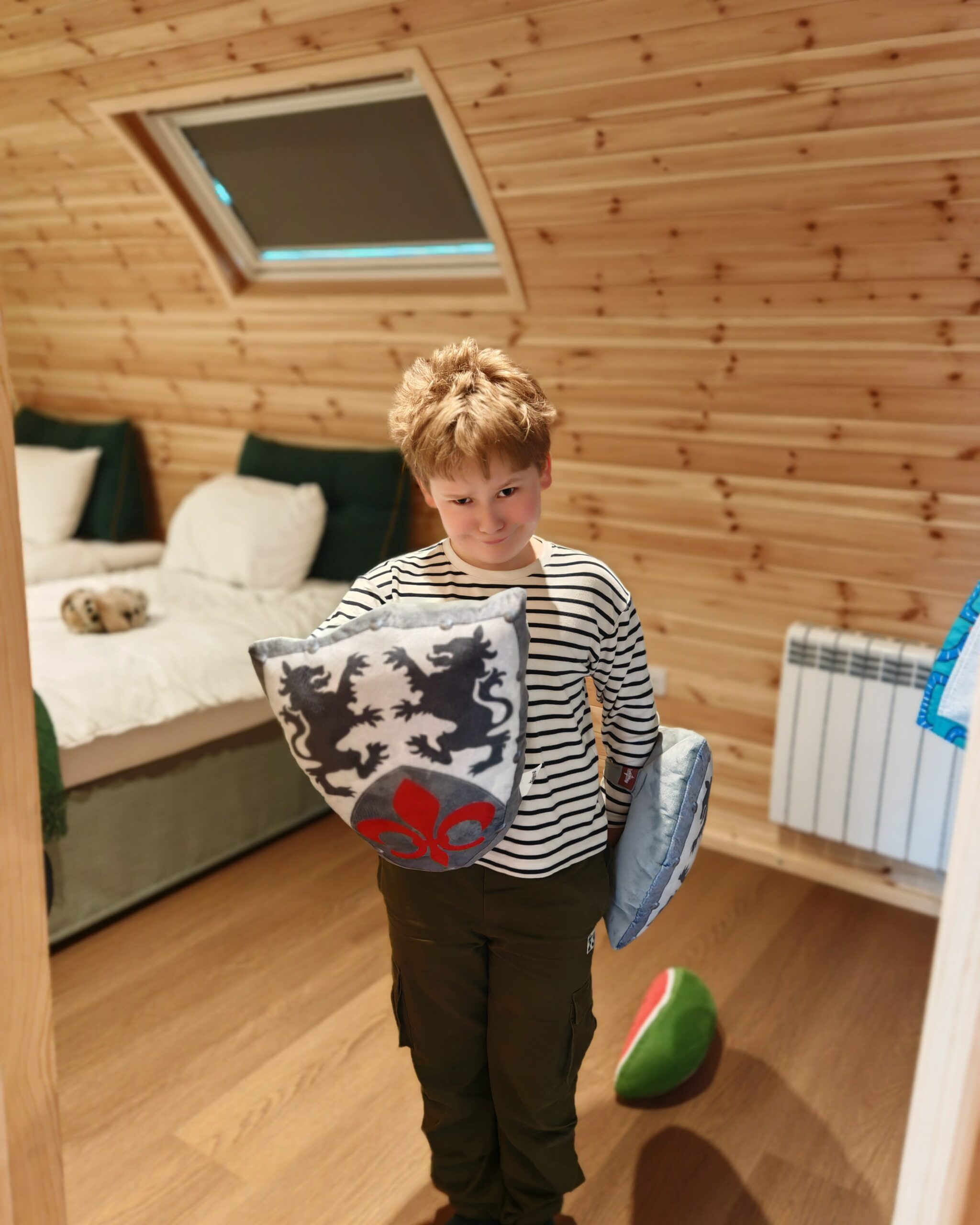 Little white boy with a stripped top in a glamping pod. He's pretending to be a knight with a soft toy in a shape of a shield Little white boy with a stripped top in a glamping pod. He's pretending to be a knight with a soft toy in a shape of a shield