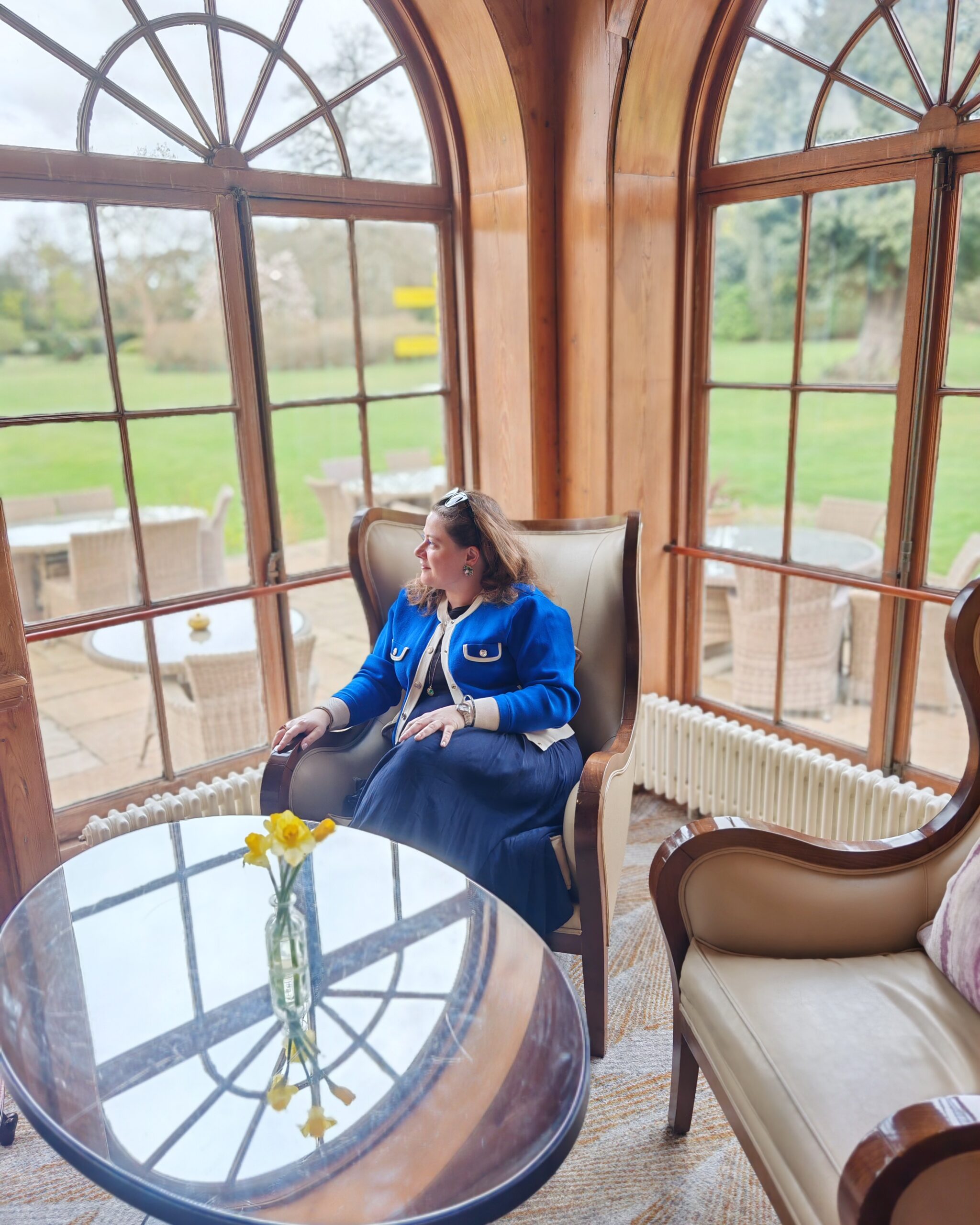 White women wearing a blue cardigan, sitting in a living-room by the windows in a an upholstered beige chair with tulips on the table. White women wearing a blue cardigan, sitting in a living-room by the windows in a an upholstered beige chair with tulips on the table.