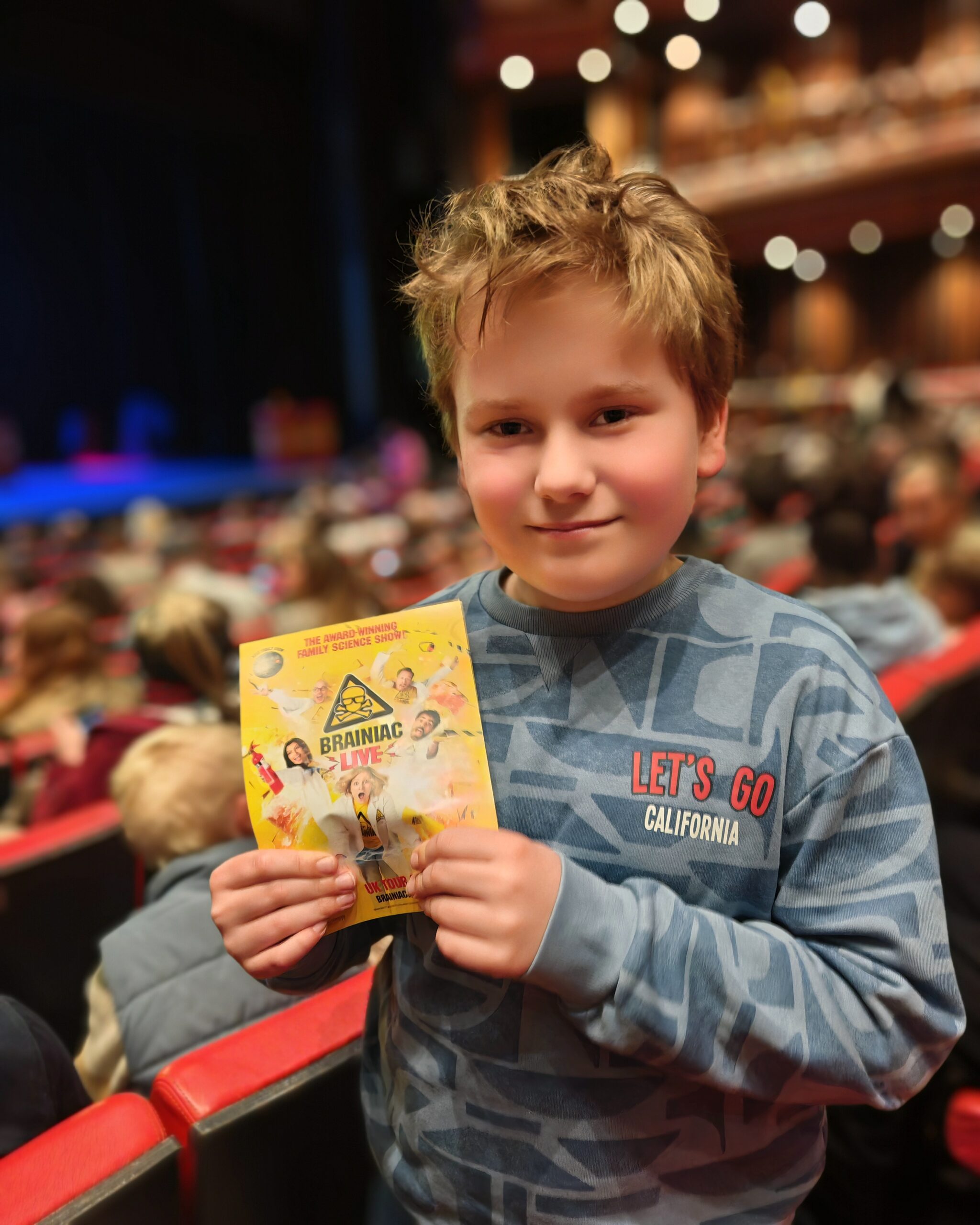 White boy wearing a blue sweater at the theatre. He's holding the leaflet for Brainiac, the educational show in the UK. White boy wearing a blue sweater at the theatre. He's holding the leaflet for Brainiac, the educational show in the UK.