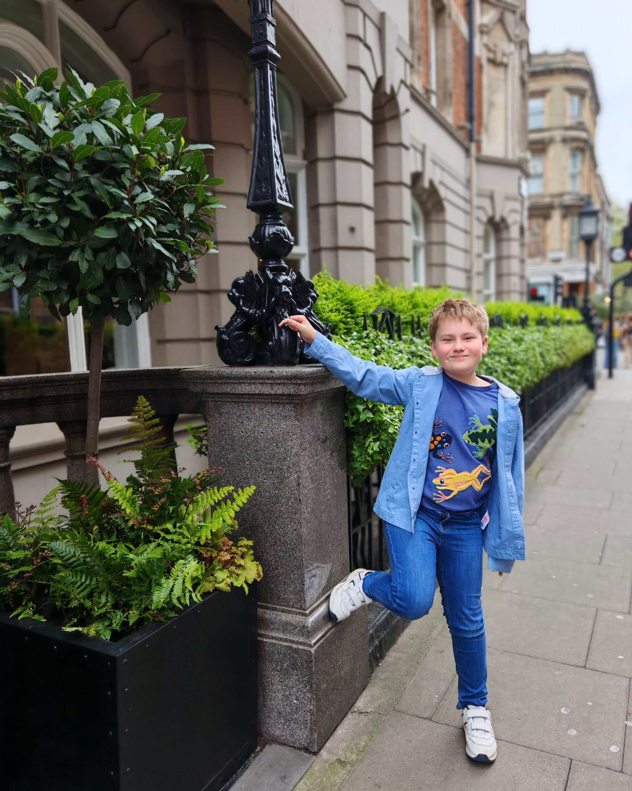 White boy wearing jeans and blue top, holding the rail of a London hotel. He is smiling and in Bloomsbury White boy wearing jeans and blue top, holding the rail of a London hotel. He is smiling and in Bloomsbury