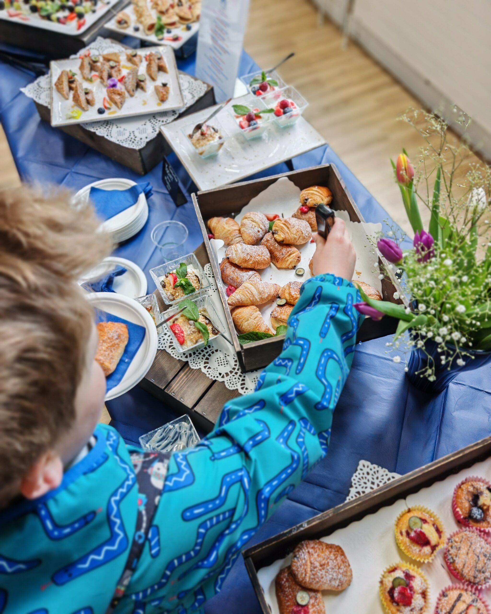 Young white boy helping himself to a breakfast spread made of croissants and other pastries. View from his shoulders Young white boy helping himself to a breakfast spread made of croissants and other pastries. View from his shoulders