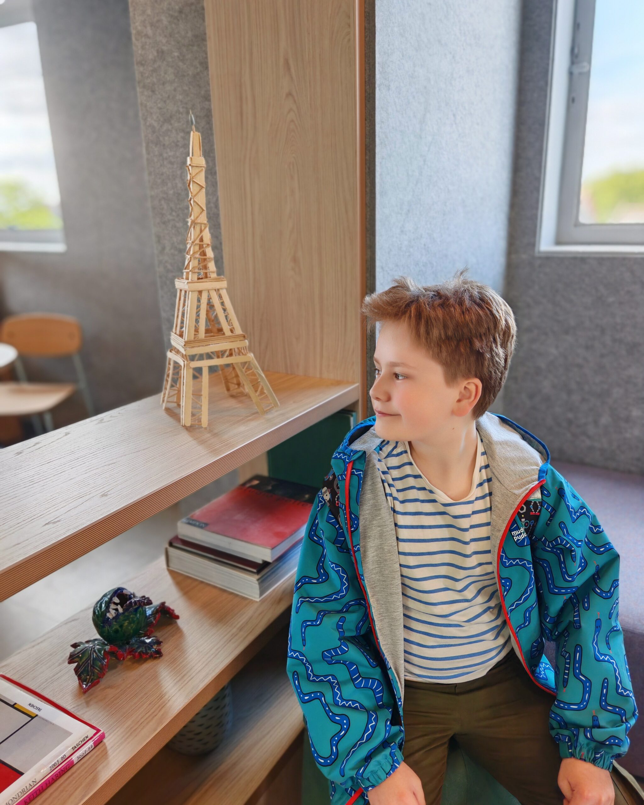Young white boy seating in a communal room in a secondary school, right by a model of the Eiffel Tower in wood Young white boy seating in a communal room in a secondary school, right by a model of the Eiffel Tower in wood