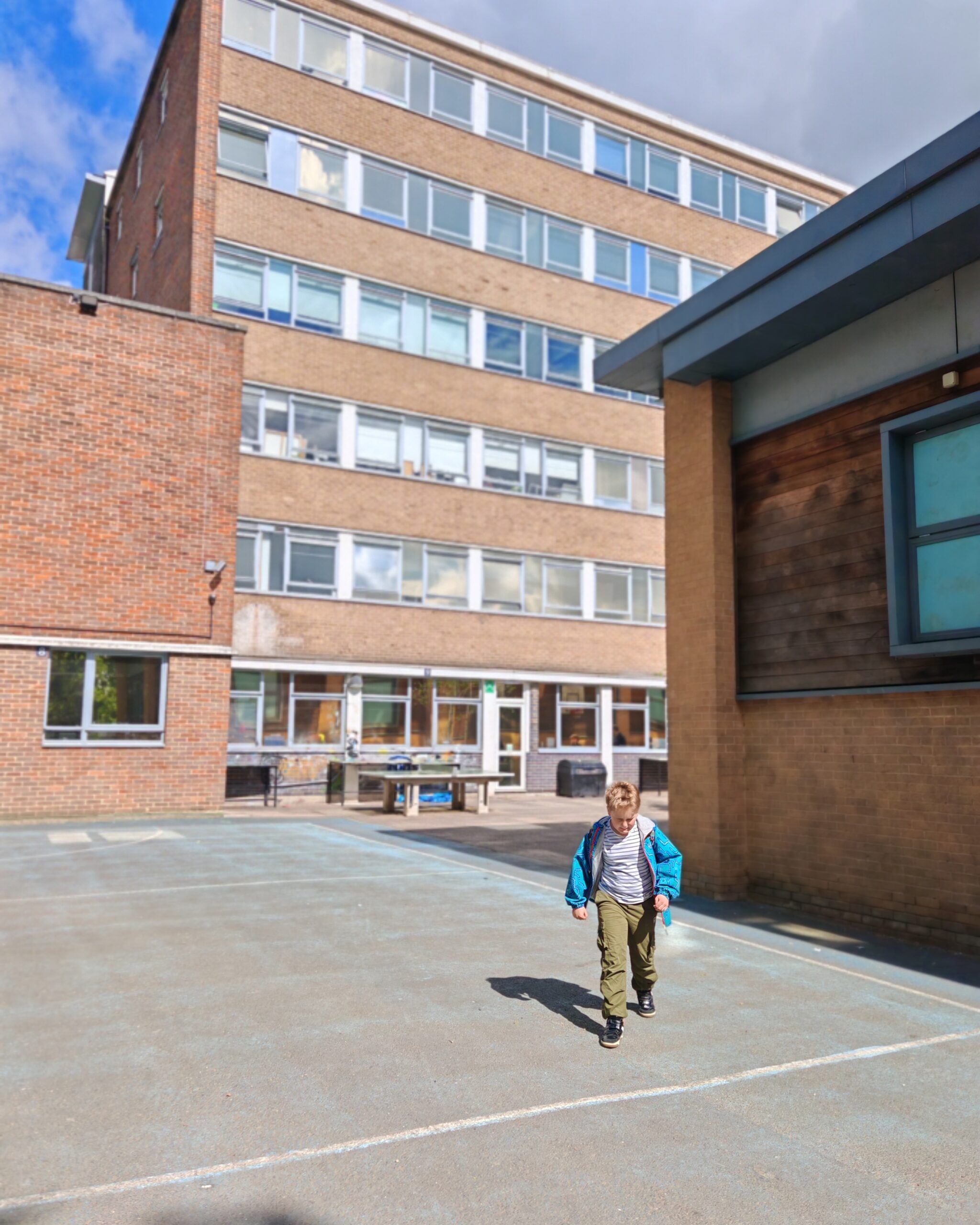 young white boy walking around a secondary school. You can see the premises behind him in the sunshine with a table tennis set up young white boy walking around a secondary school. You can see the premises behind him in the sunshine with a table tennis set up