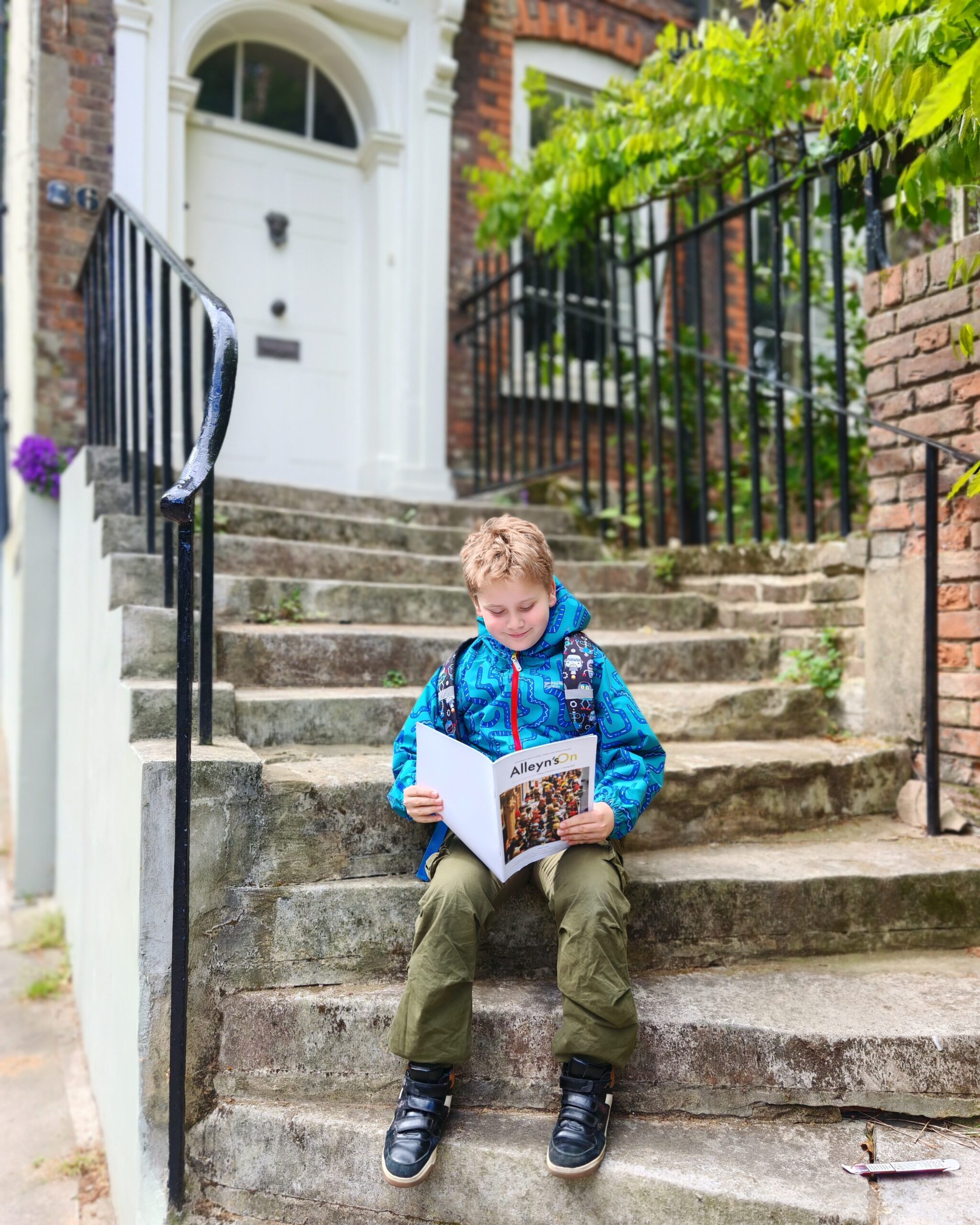 White little boy sitting on a doorstep in Hampstead, North London. He's reading the brochure for Alleyn's School Group after visiting the local school