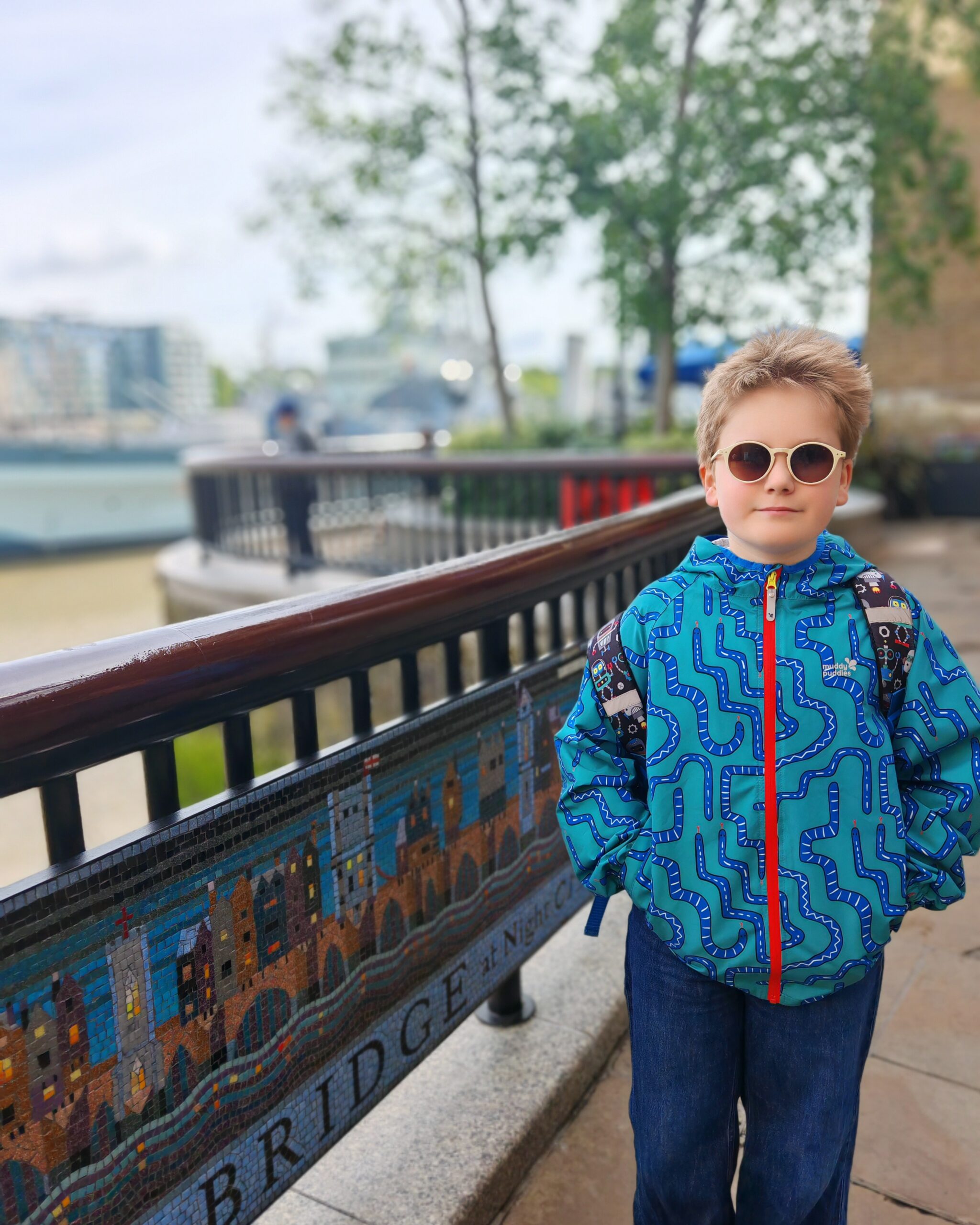 White little boy with a blue raincoat, walking along the Bank in London. He has his hands in his pockets and he's wearing white sunglasses White little boy with a blue raincoat, walking along the Bank in London. He has his hands in his pockets and he's wearing white sunglasses