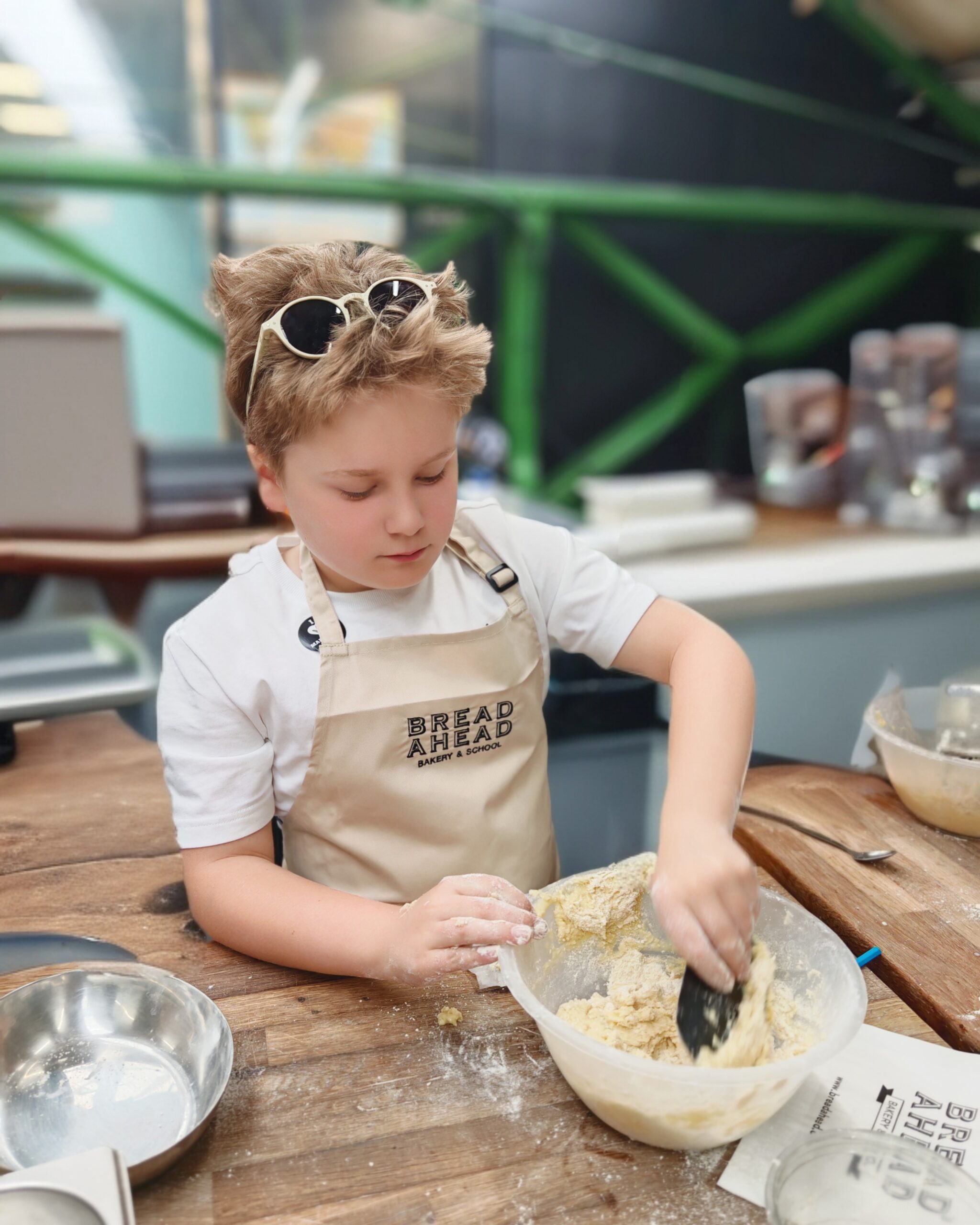 White little boy taking a baking class with Bread Ahead in London. He's preparing some scones while wearing the brand's apron White little boy taking a baking class with Bread Ahead in London. He's preparing some scones while wearing the brand's apron
