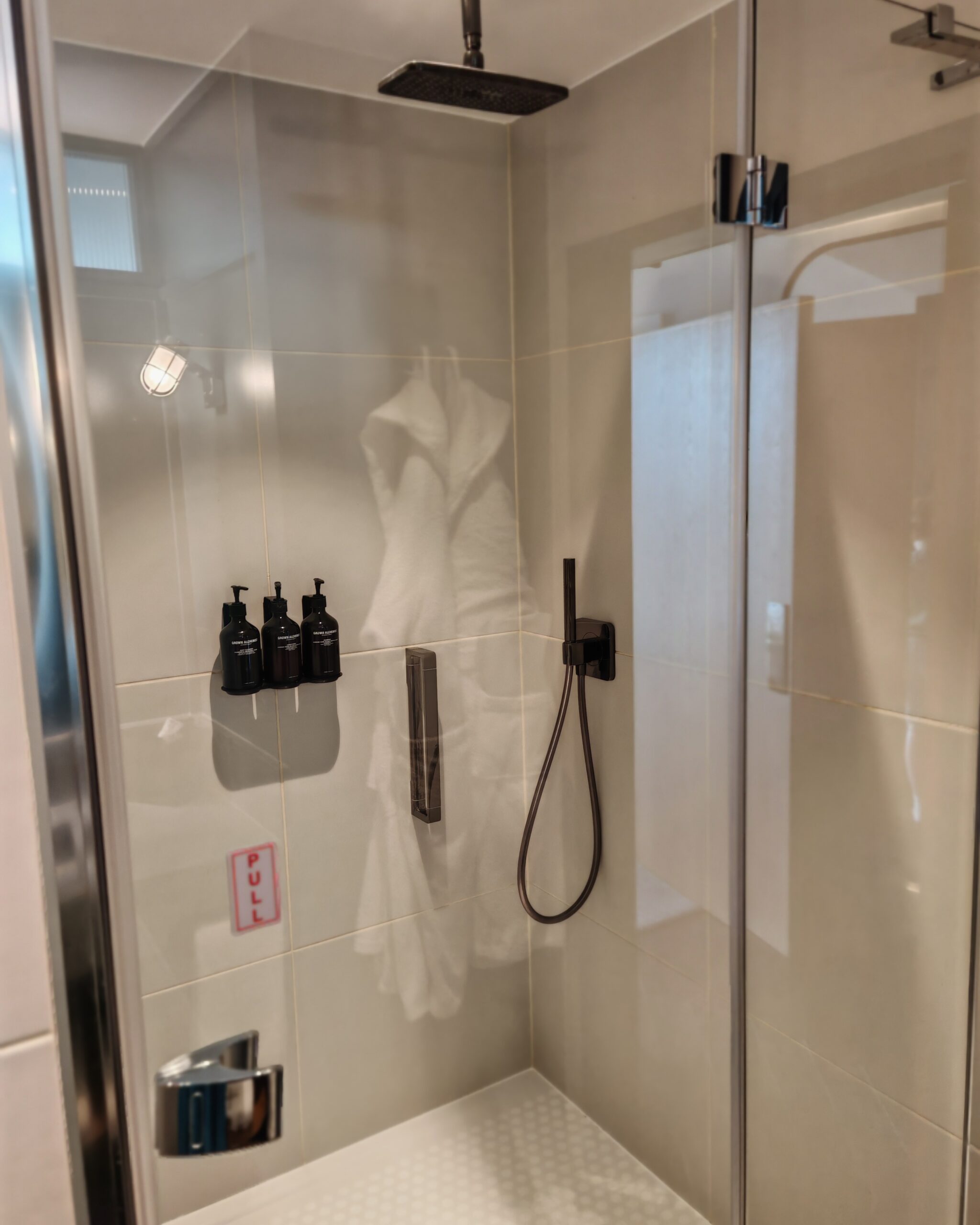 Shower room at the Gantry Hotel in London with a white spacious shower and toiletries included on the inside wall.