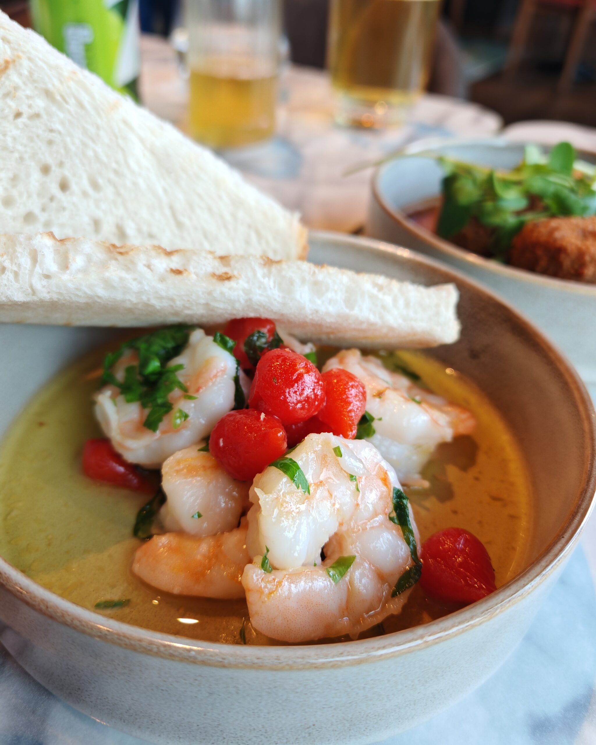 Photo of prawns with some tomatoes served in a small grey plate with some bread on top of it.