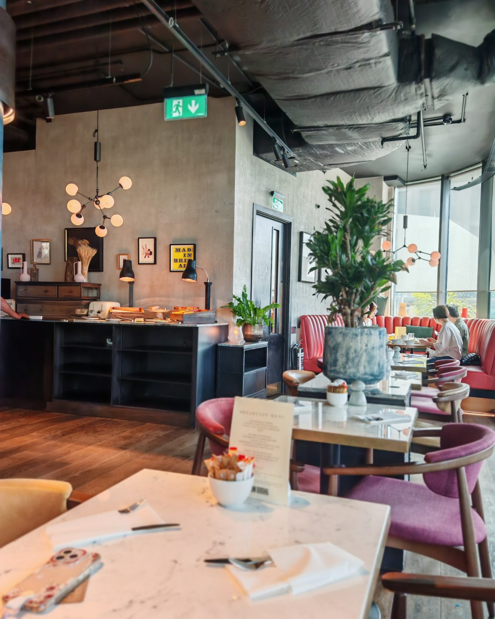 Breakfast area at the Gantry Hotel with chairs and a part of the cold buffet. Some people are seating on the back round chair