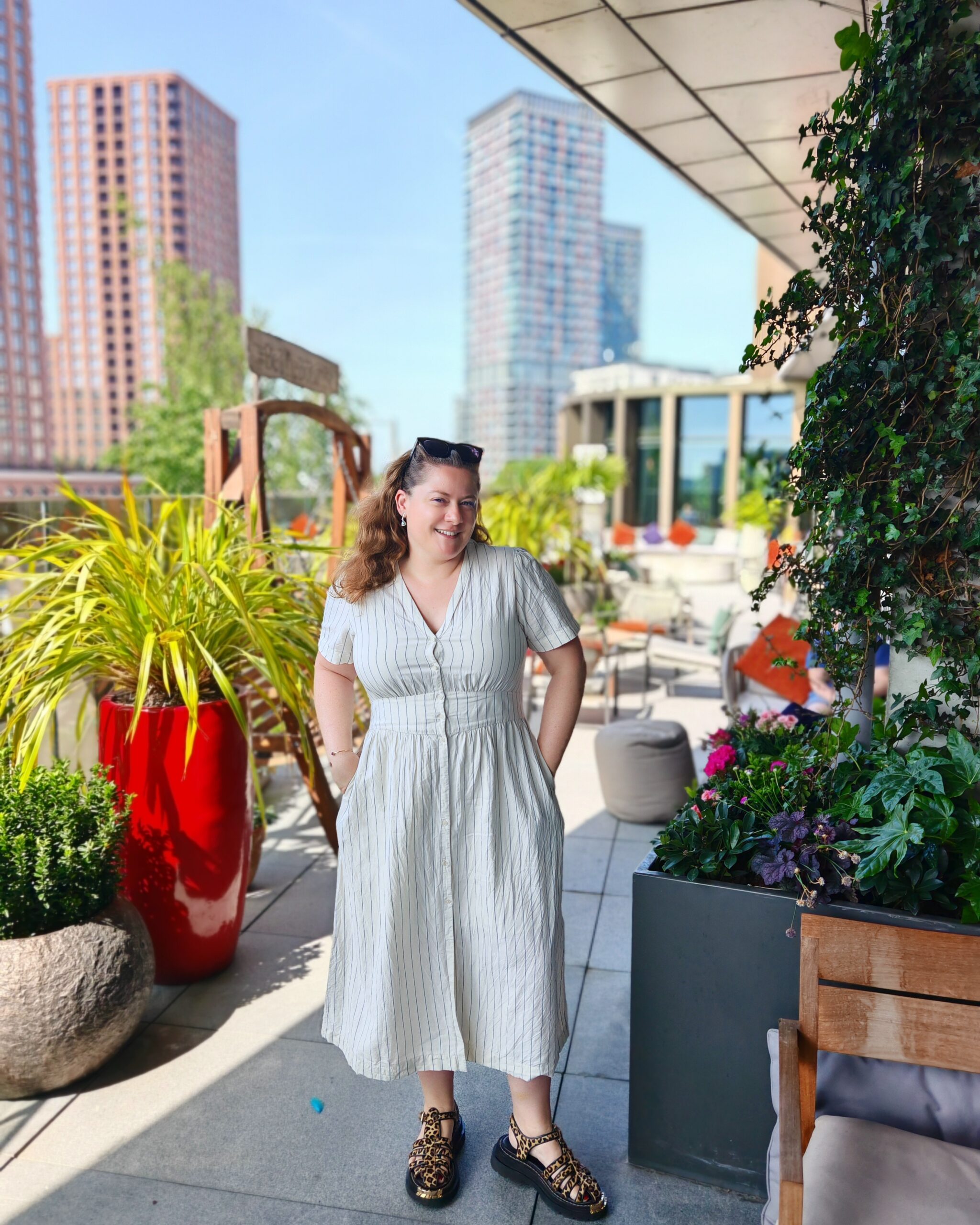 White woman wearing a linen white dress while standing in an urban jungle at the Gantry Hotel in Stratford White woman wearing a linen white dress while standing in an urban jungle at the Gantry Hotel in Stratford