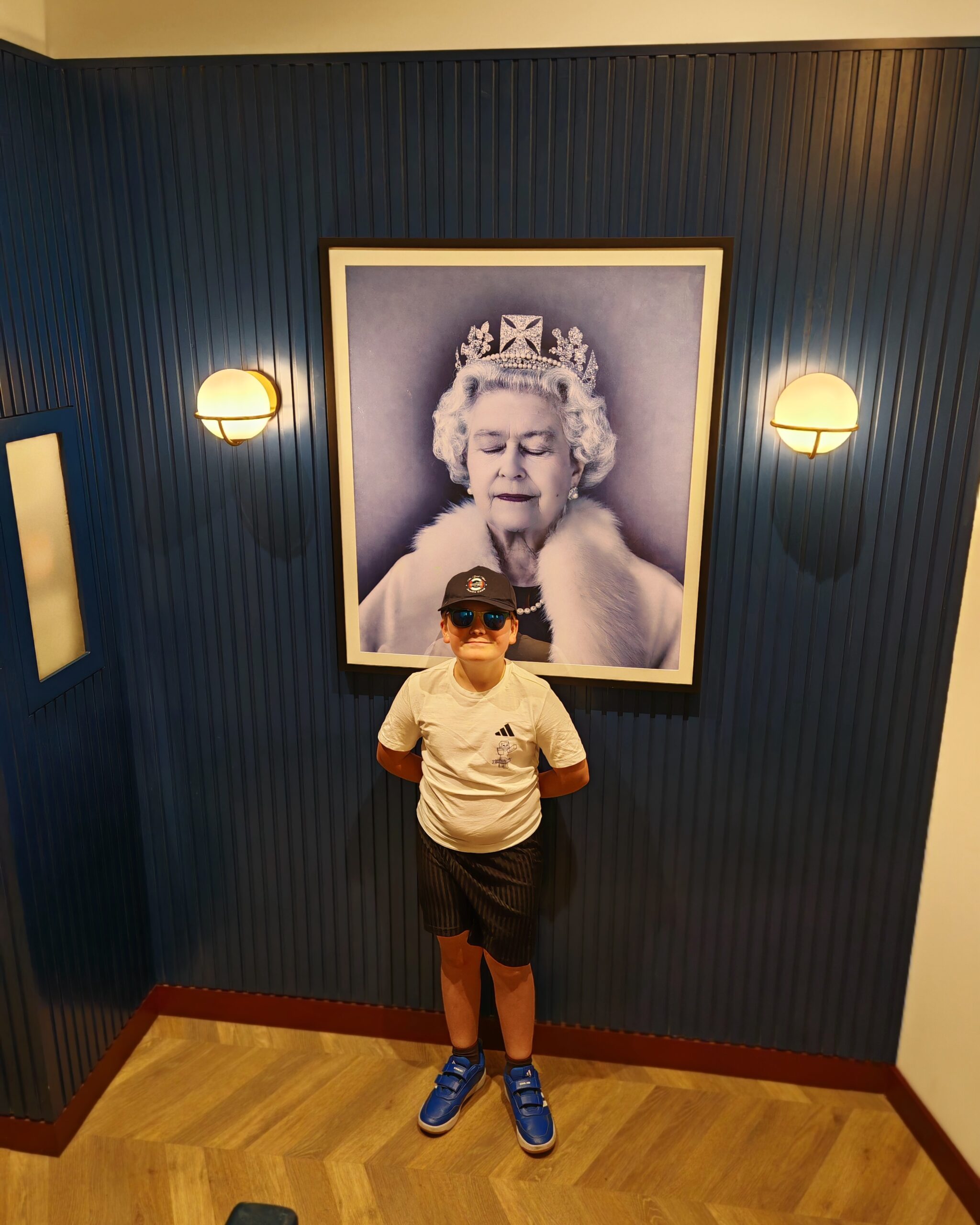 white little boy standing in by a modern portrait of Queen Elizabeth II inside the lobby of Onefifty Fenchurch, a new aparthotel in the heart of London white little boy standing in by a modern portrait of Queen Elizabeth II inside the lobby of Onefifty Fenchurch, a new aparthotel in the heart of London