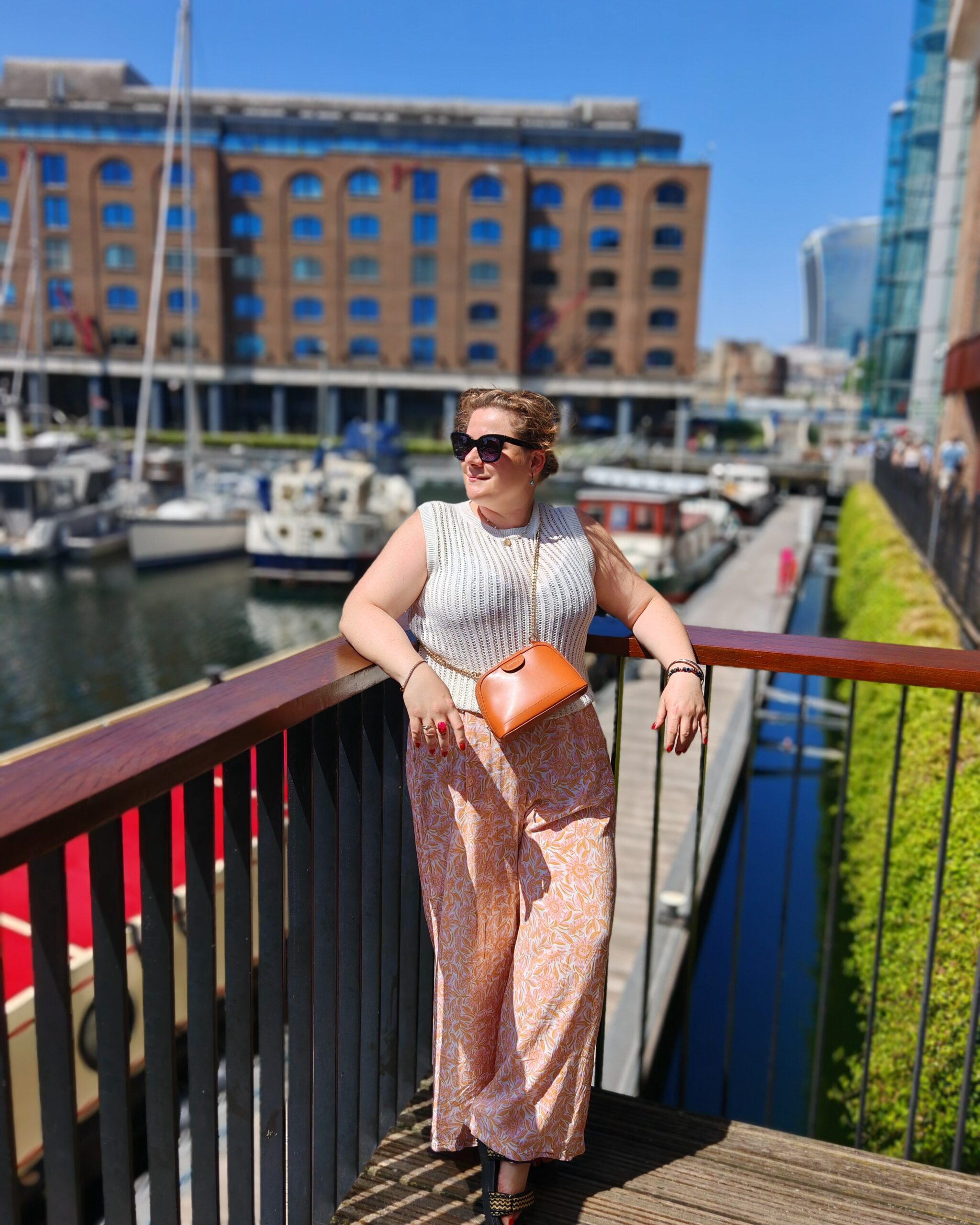 White woman wearing a crochet top and pink trousers standing by St Katherine Docks in London White woman wearing a crochet top and pink trousers standing by St Katherine Docks in London