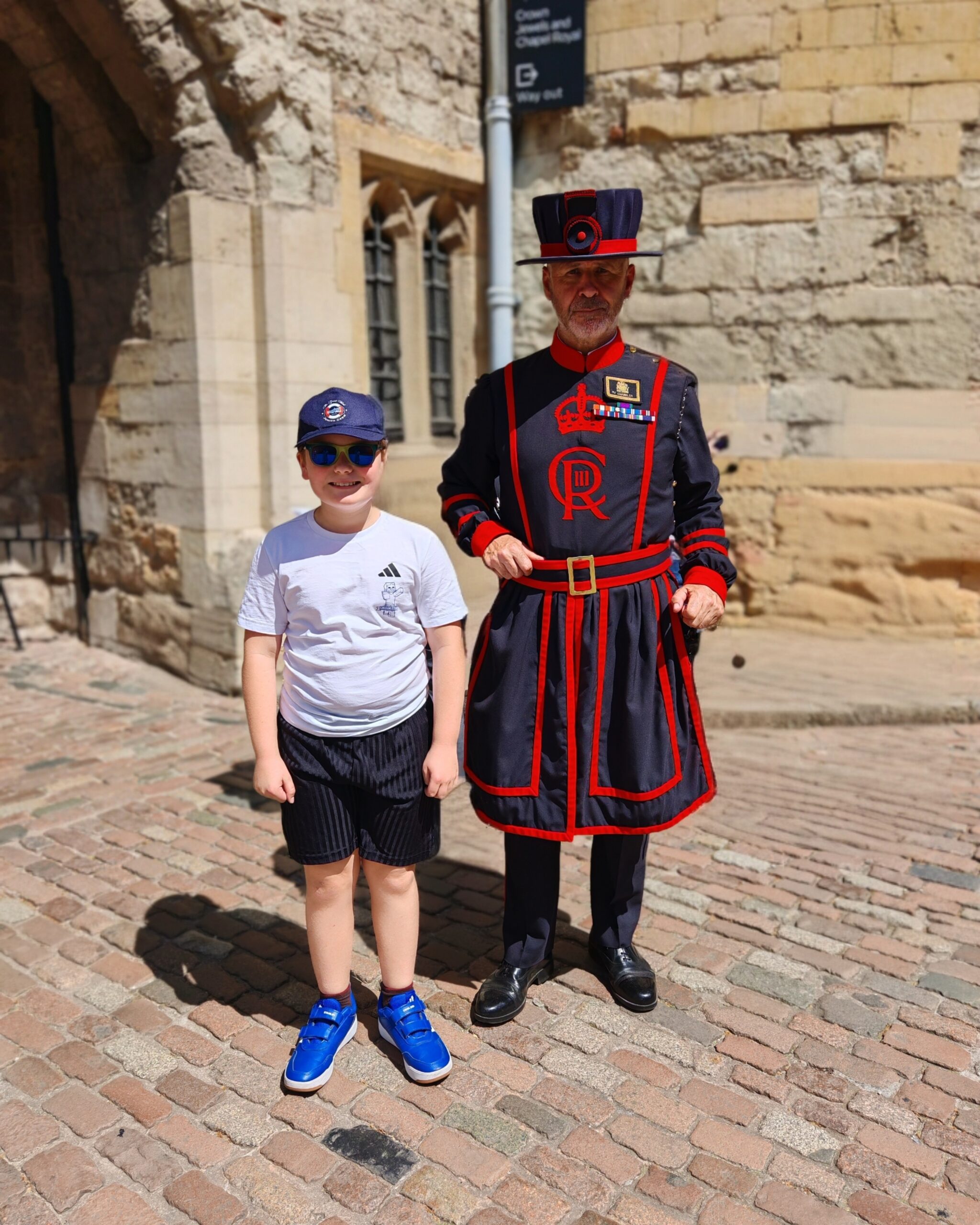 white little boy with black shorts and a white tee standing right next to a Beefeaters outside Tower of London. white little boy with black shorts and a white tee standing right next to a Beefeaters outside Tower of London.