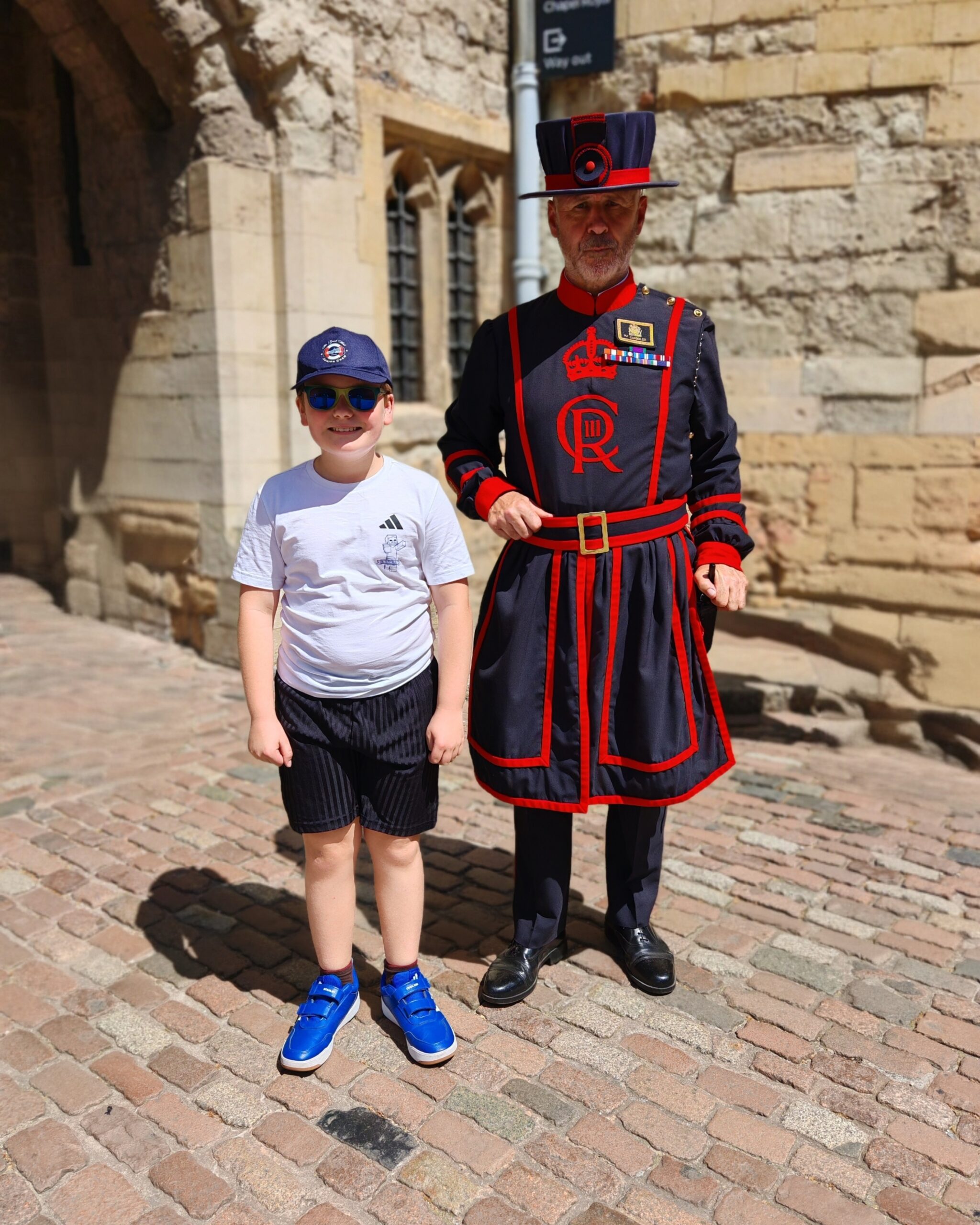 white little boy with a white tee and black shorts posing for a photo with a Beefeater at the Tower of London white little boy with a white tee and black shorts posing for a photo with a Beefeater at the Tower of London