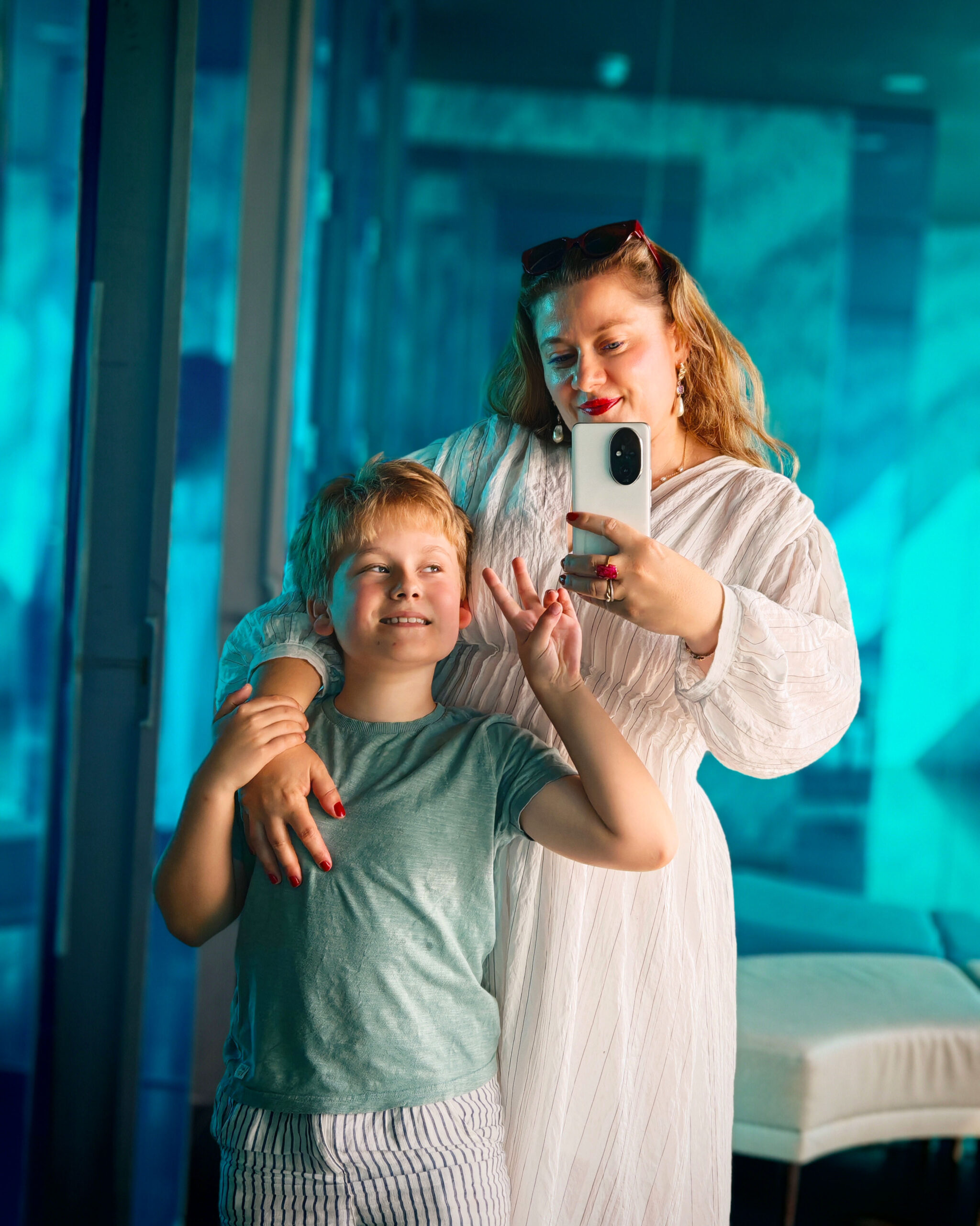 White woman in a white linen dress posing for a selfie with her son in front of the mirror of a London restaurant in London