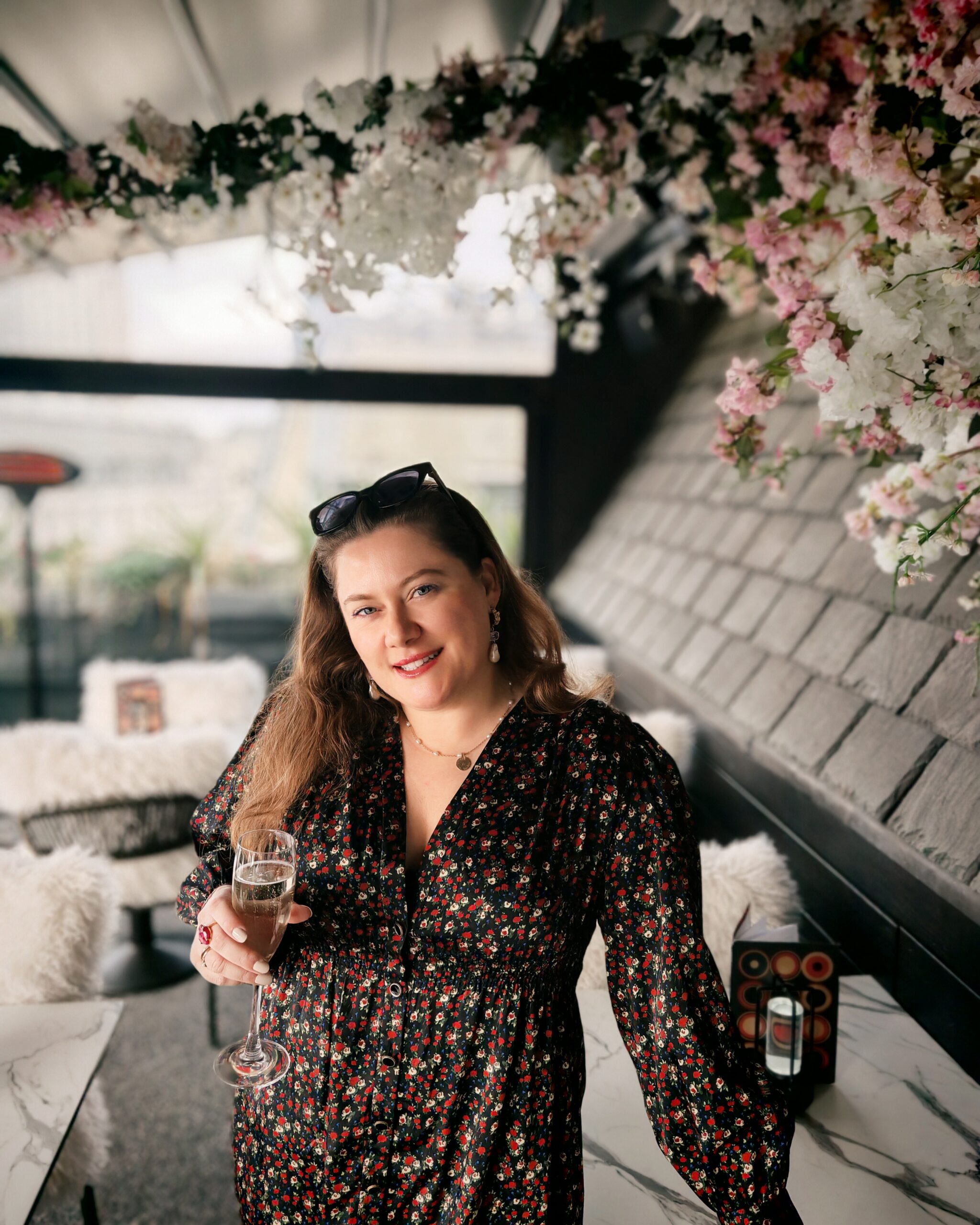 White woman in a black flowery dress standing at the terrace of Aqua Kyoto in Carnaby Street in London, with a glass of champagne. White woman in a black flowery dress standing at the terrace of Aqua Kyoto in Carnaby Street in London, with a glass of champagne.