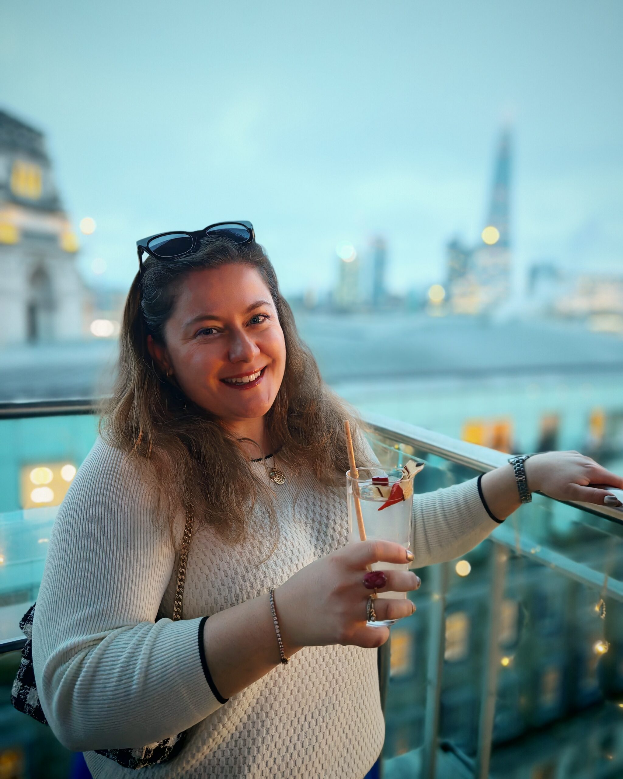 White woman holding a cocktail while standing on Savage Garden Rooftop Bar in London. You can see the Shard in the background White woman holding a cocktail while standing on Savage Garden Rooftop Bar in London. You can see the Shard in the background