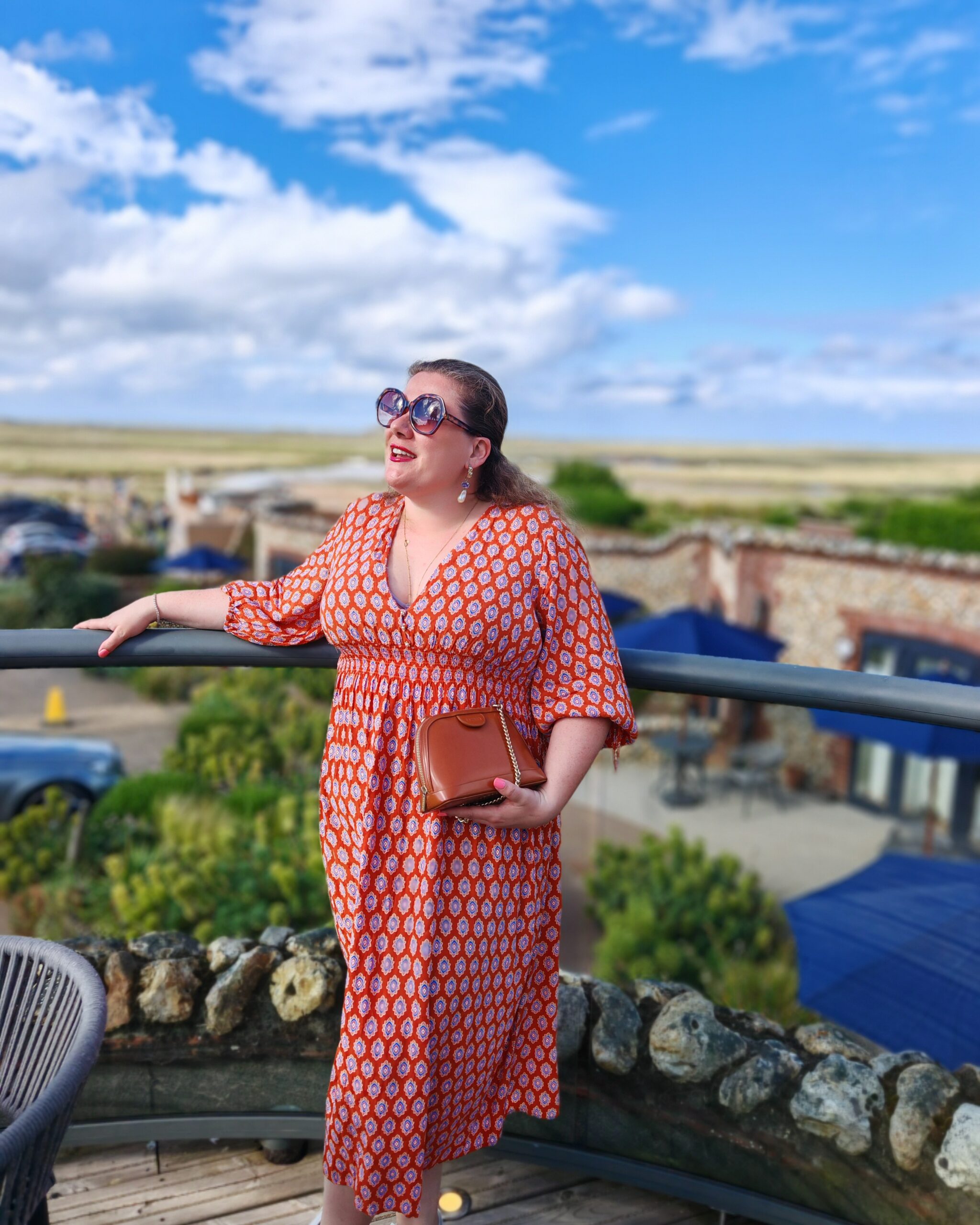 White woman in bright orange dress standing on the balcony of a restaurant in Brancaster, on the Norfolk Coast White woman in bright orange dress standing on the balcony of a restaurant in Brancaster, on the Norfolk Coast