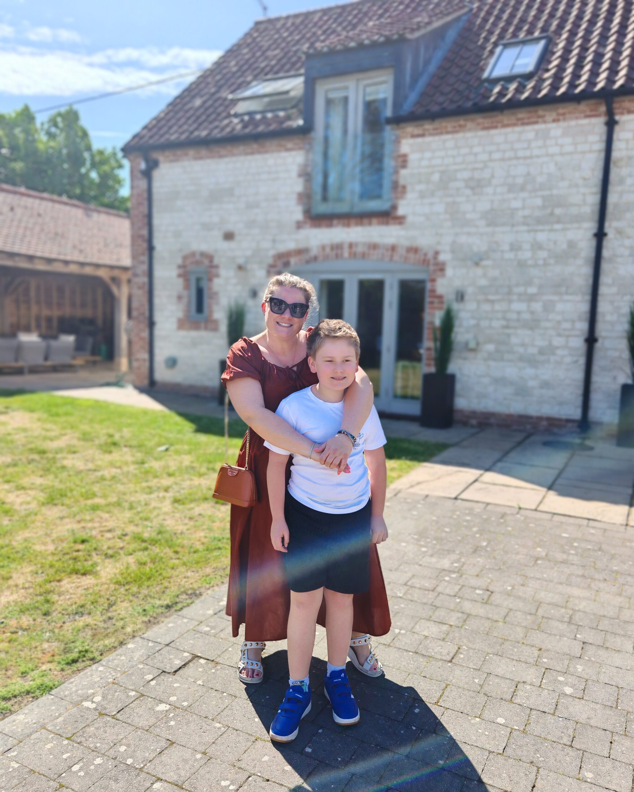 White woman in a brown dress with her son standing in front of 4 Manor Farm Barns in Brancaster, Norfolk with Barefoot Retreats White woman in a brown dress with her son standing in front of 4 Manor Farm Barns in Brancaster, Norfolk with Barefoot Retreats