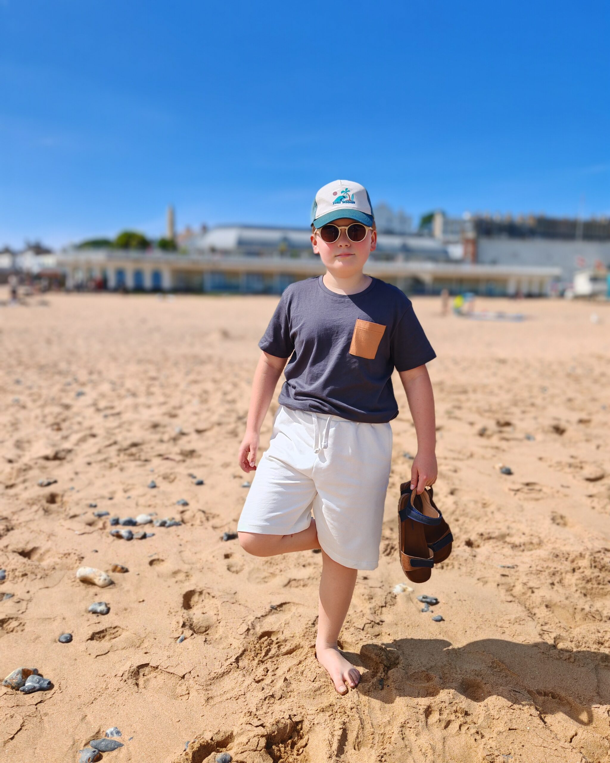 White little boy in white shorts and grey tee-shirts playing on the beach of Ramsgate. You can see the Royal Victoria Pavilion in the background White little boy in white shorts and grey tee-shirts playing on the beach of Ramsgate. You can see the Royal Victoria Pavilion in the background