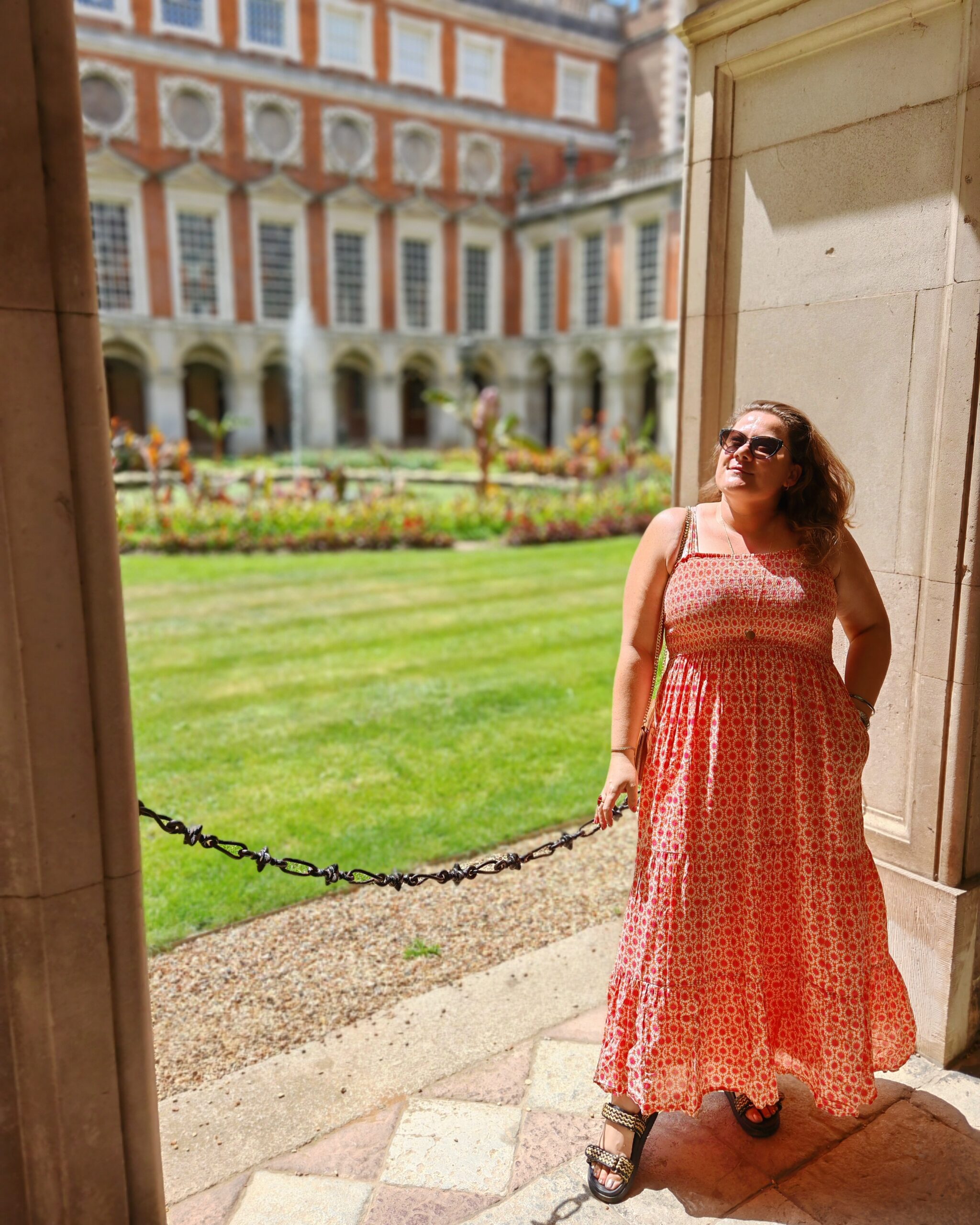White woman wearing a long orange summer dress standing by the Fountain Court at Hampton Court Palace in South West London 