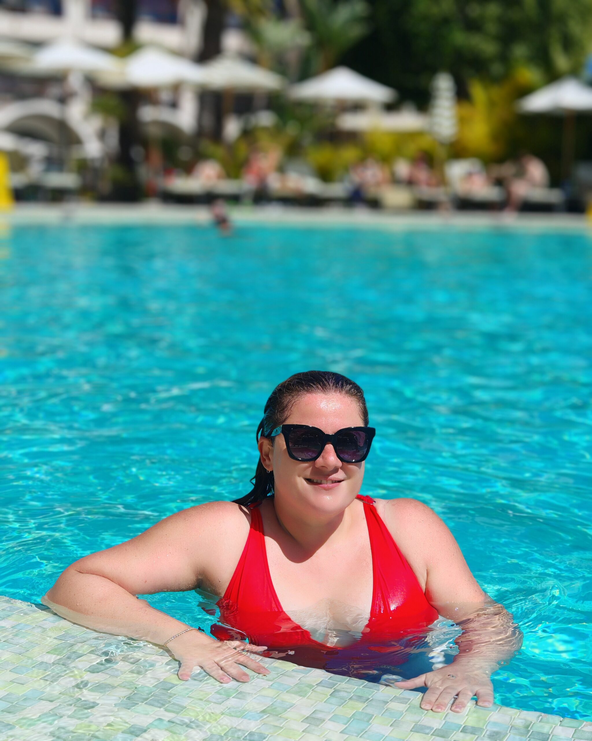 White woman in a red swimsuit, posing in the main pool the Seaside Sandy Beach Hotel