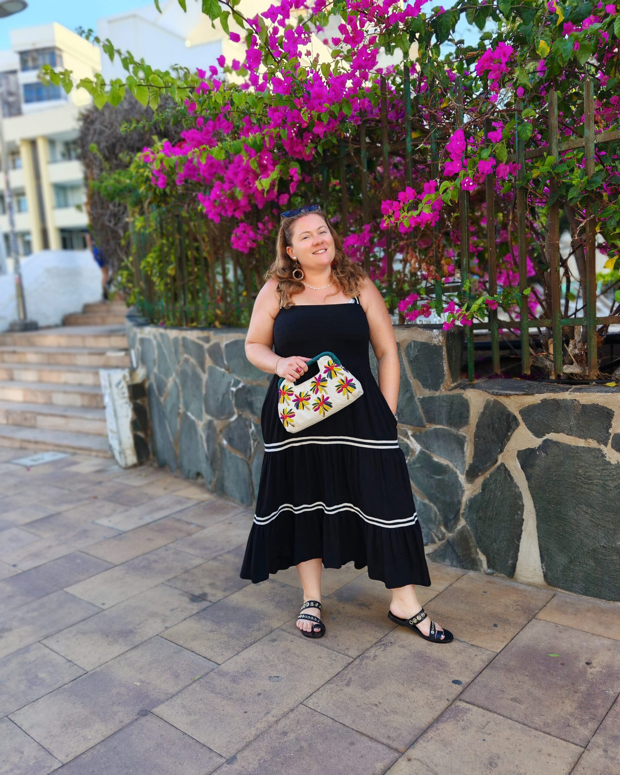 white woman in a long black dress and floral bag pouch in Gran Canaria by some pink bougainvillea