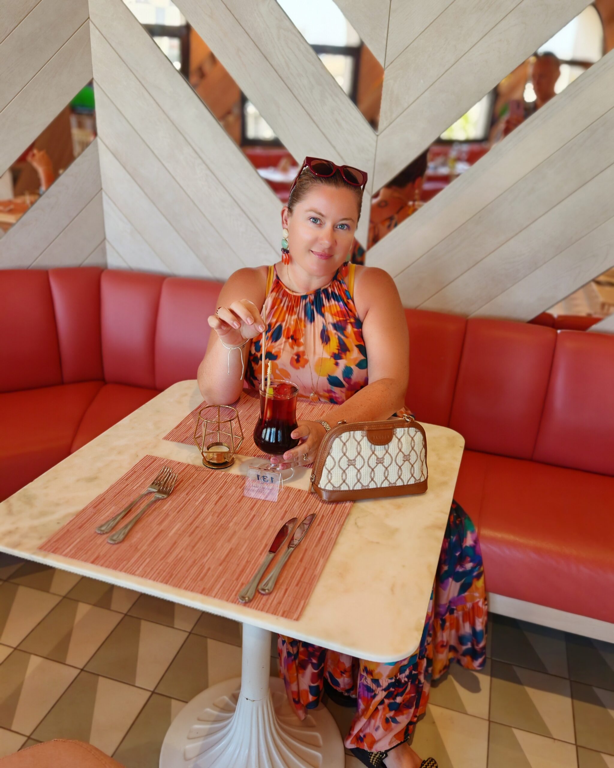White woman at the Seaside Sandy Beach Hotel main restaurant with a sangria in her hands and a small beige handbag on the table