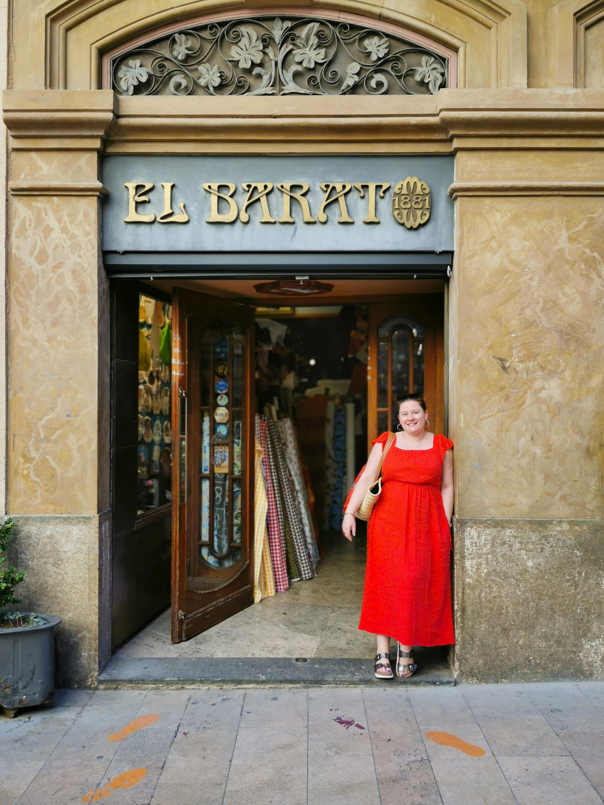White woman in a bright red dress standing in front of the El Barato, the historic family-run textile and fabric shop in the heart of Reus, Spain White woman in a bright red dress standing in front of the El Barato, the historic family-run textile and fabric shop in the heart of Reus, Spain