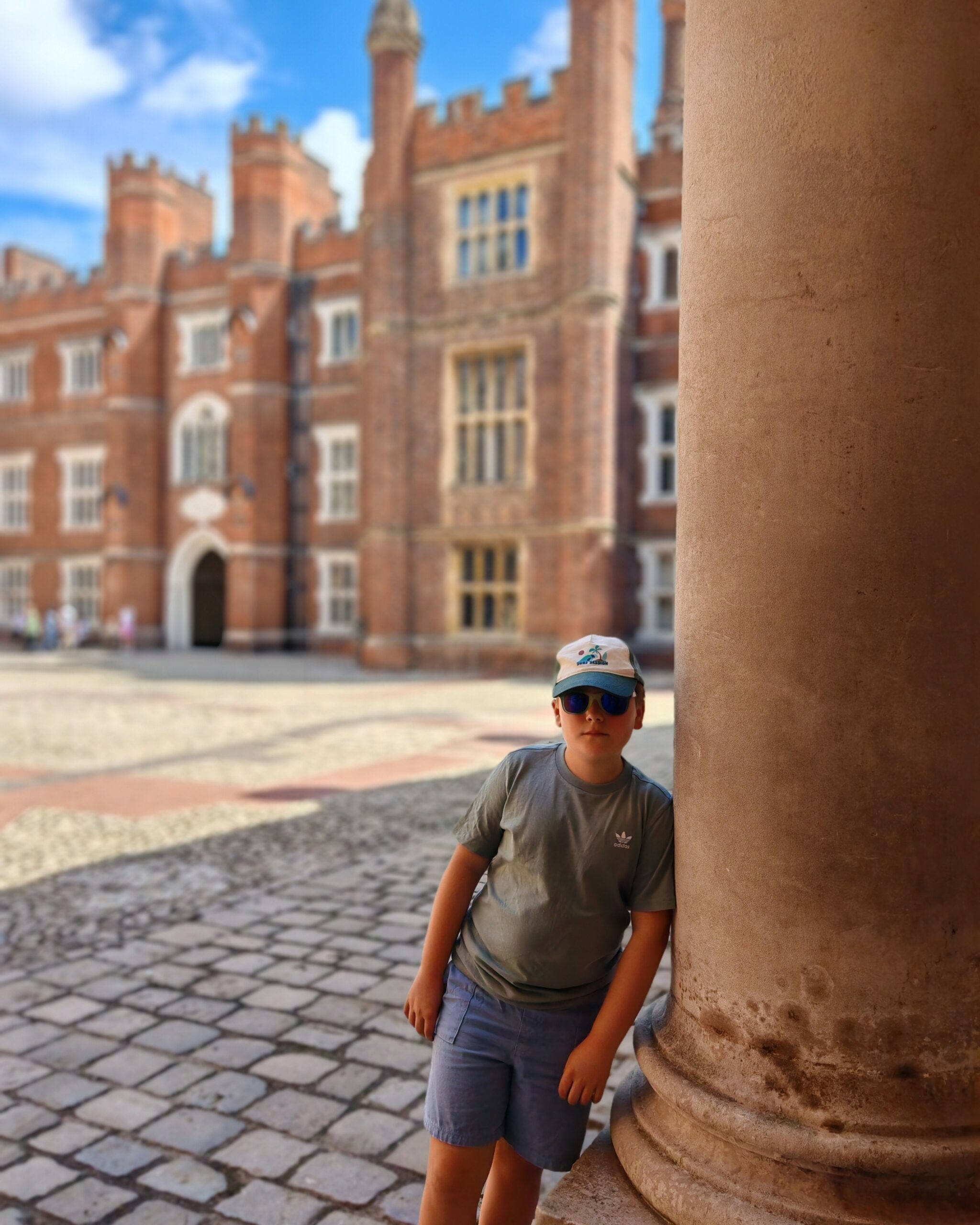 White little boy with a green tee and a cap, standing by the inside court of Hampton Court Palace in south-West London
