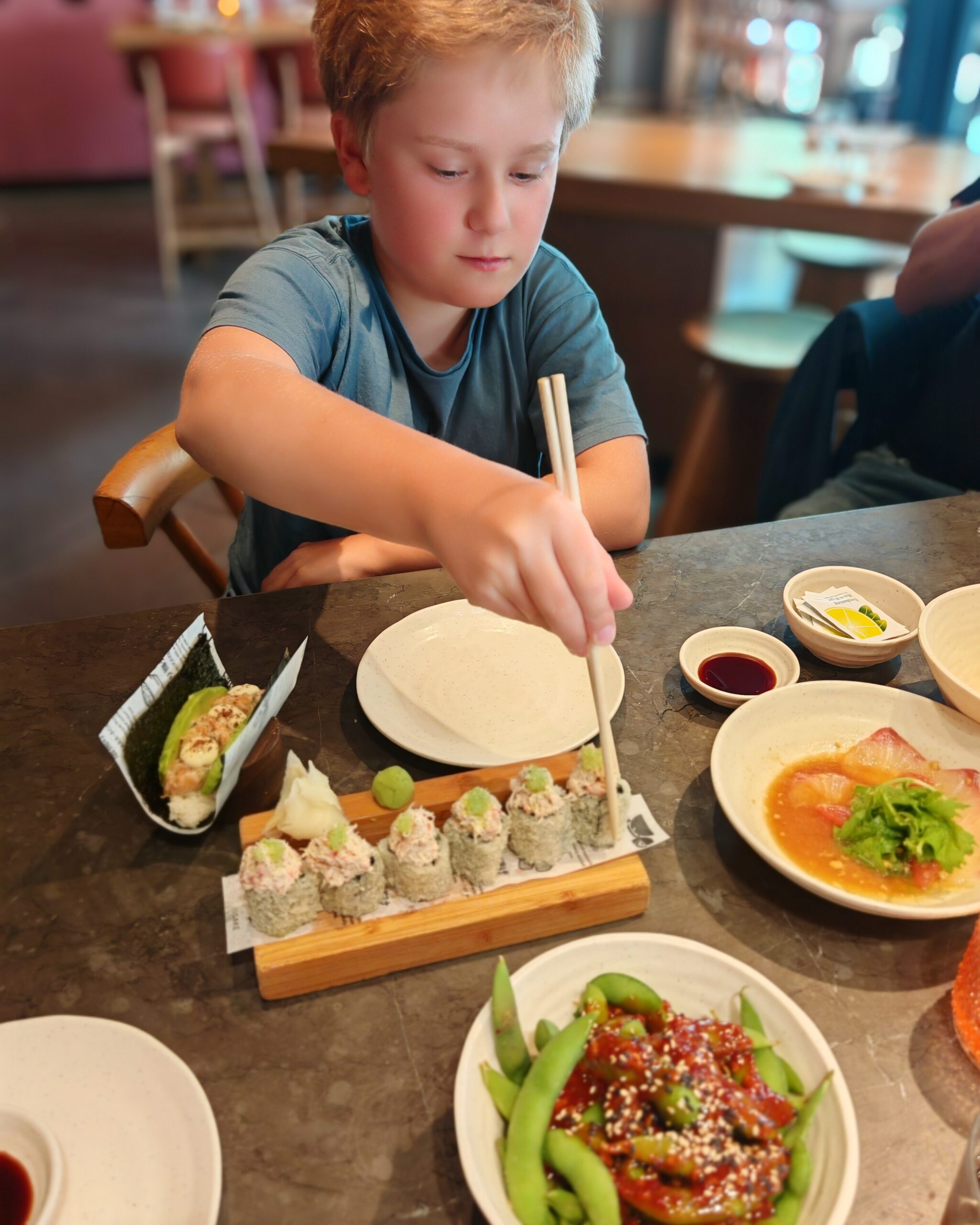 White little boy at Inko Sushi in London. He's helping himself with California Maki rolls with his sticks