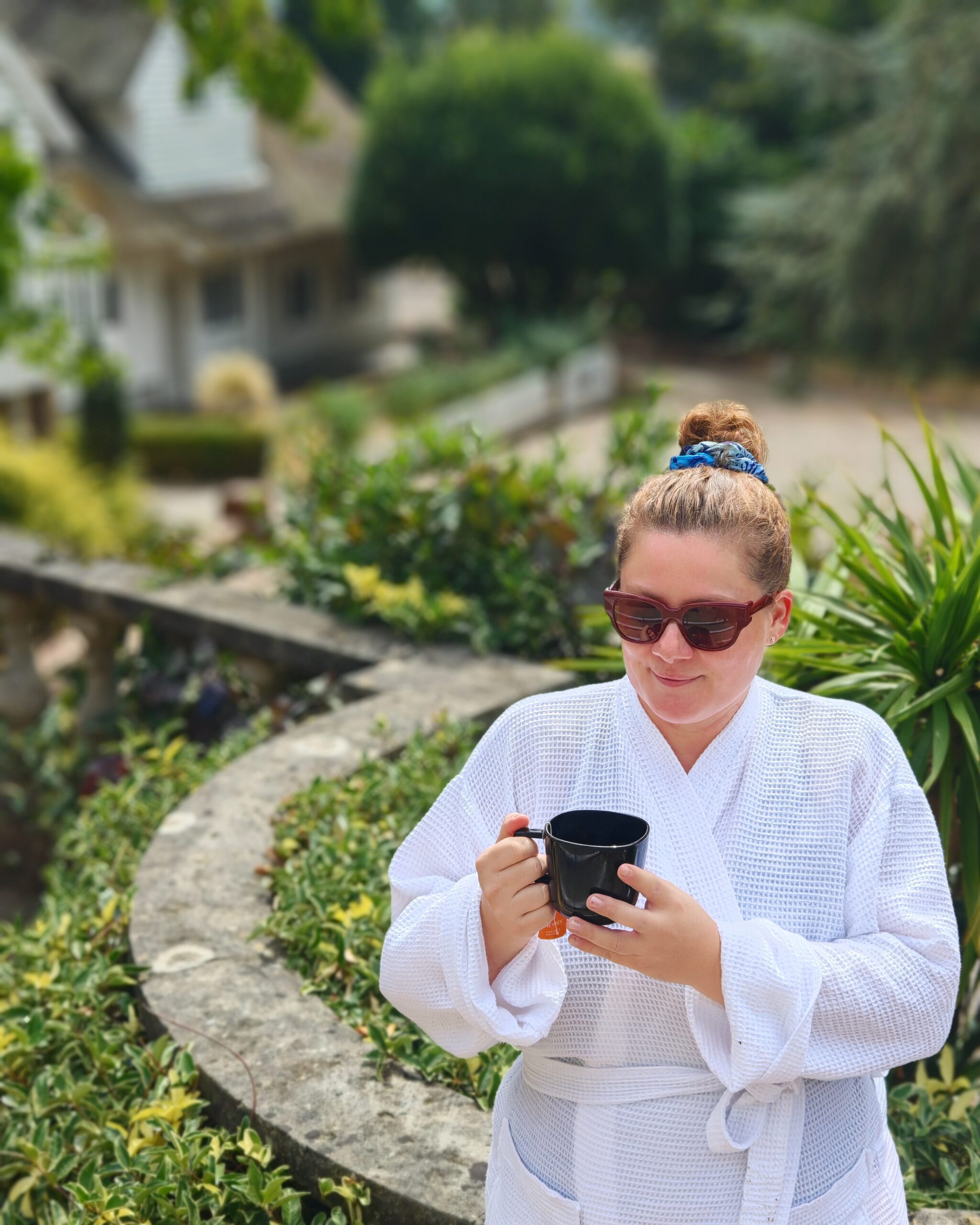 White woman in a white robe with a mum bun holding a cup of coffee in the grounds of Rowhill Grange Spa Utopia in Kent White woman in a white robe with a mum bun holding a cup of coffee in the grounds of Rowhill Grange Spa Utopia in Kent