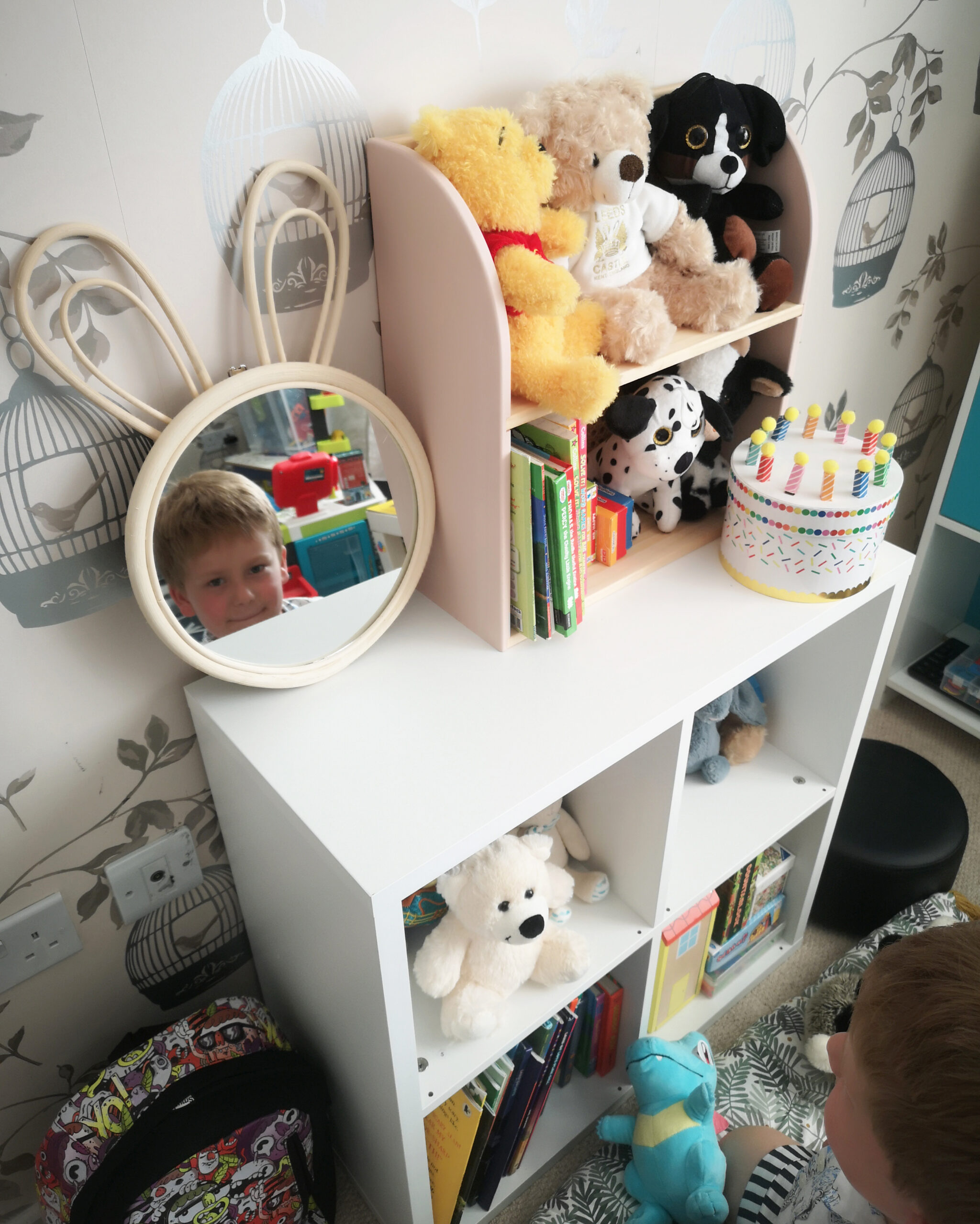 Storage shelf in white in a kids' bedroom, filled with soft toys, books and a birthday cake box on top of it. Storage shelf in white in a kids' bedroom, filled with soft toys, books and a birthday cake box on top of it.