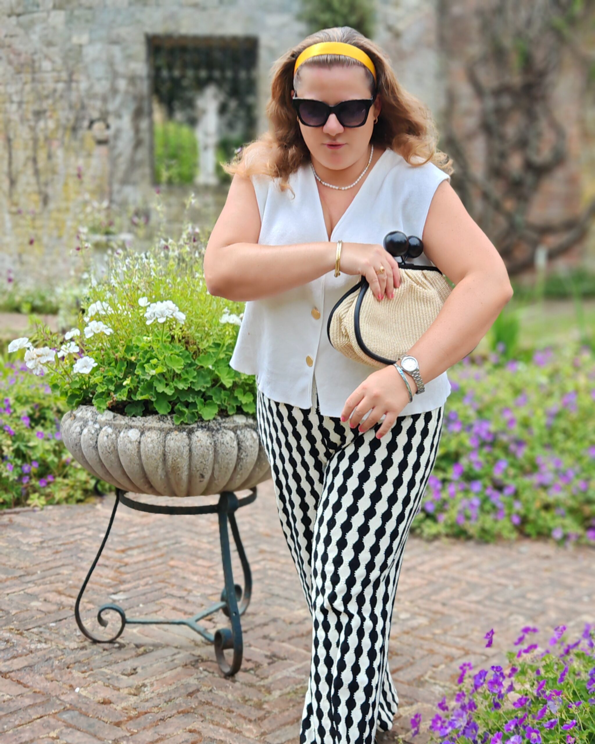 white woman in a beige vest top and a black and white pair of trousers walking around an English garden in Kent. It's one of the outdoors gardens at Eastwell Manor near Ashford in Kent white woman in a beige vest top and a black and white pair of trousers walking around an English garden in Kent. It's one of the outdoors gardens at Eastwell Manor near Ashford in Kent
