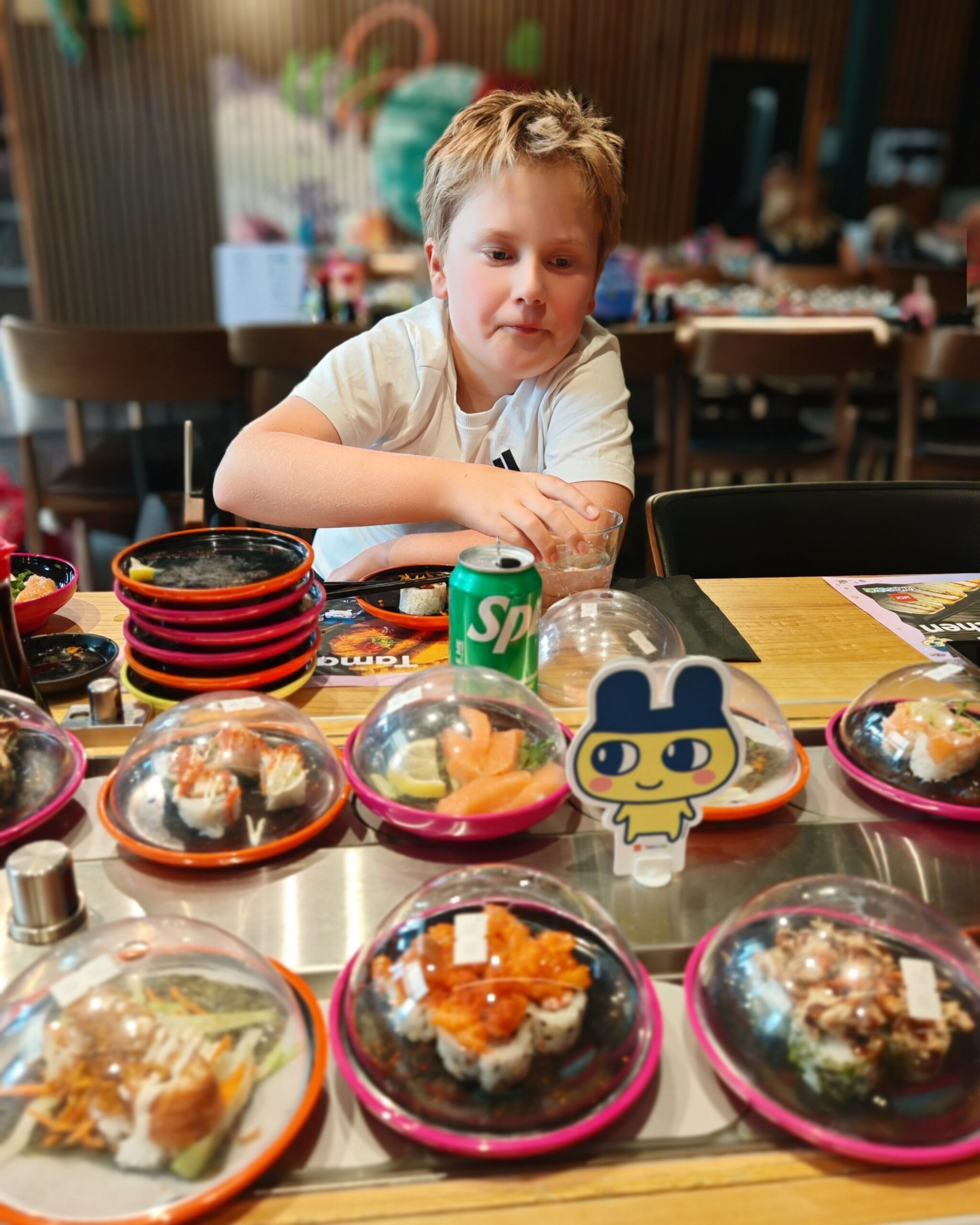 White little boy with blond hair wearing a white tee with an array of sushi plates in front of him during the bottomless brunch at Yo Sushi at the Ashford Designer Outlet