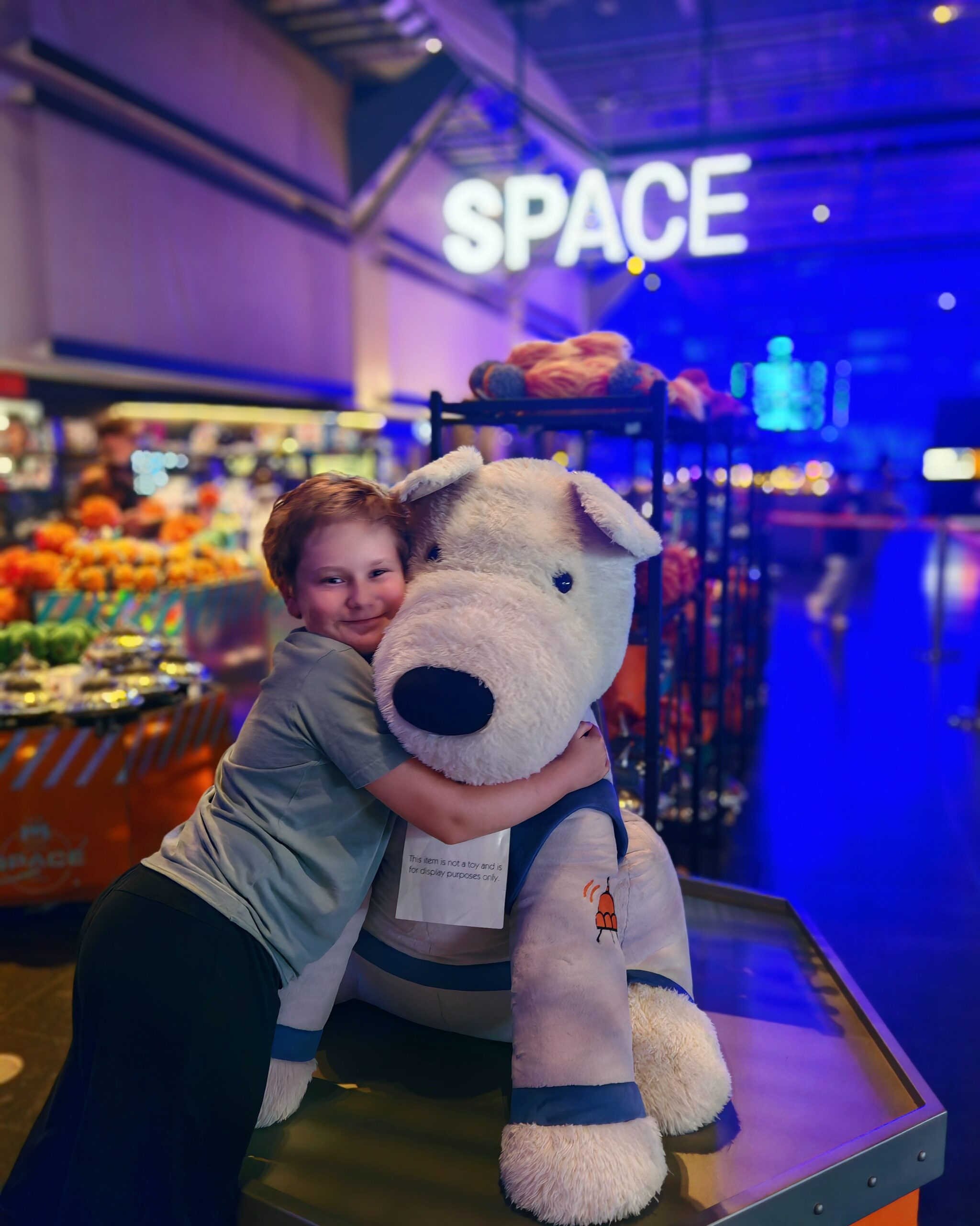White little boy with a green tee-shirt squeezing a huge teddy in the space section at the Science Museum in London