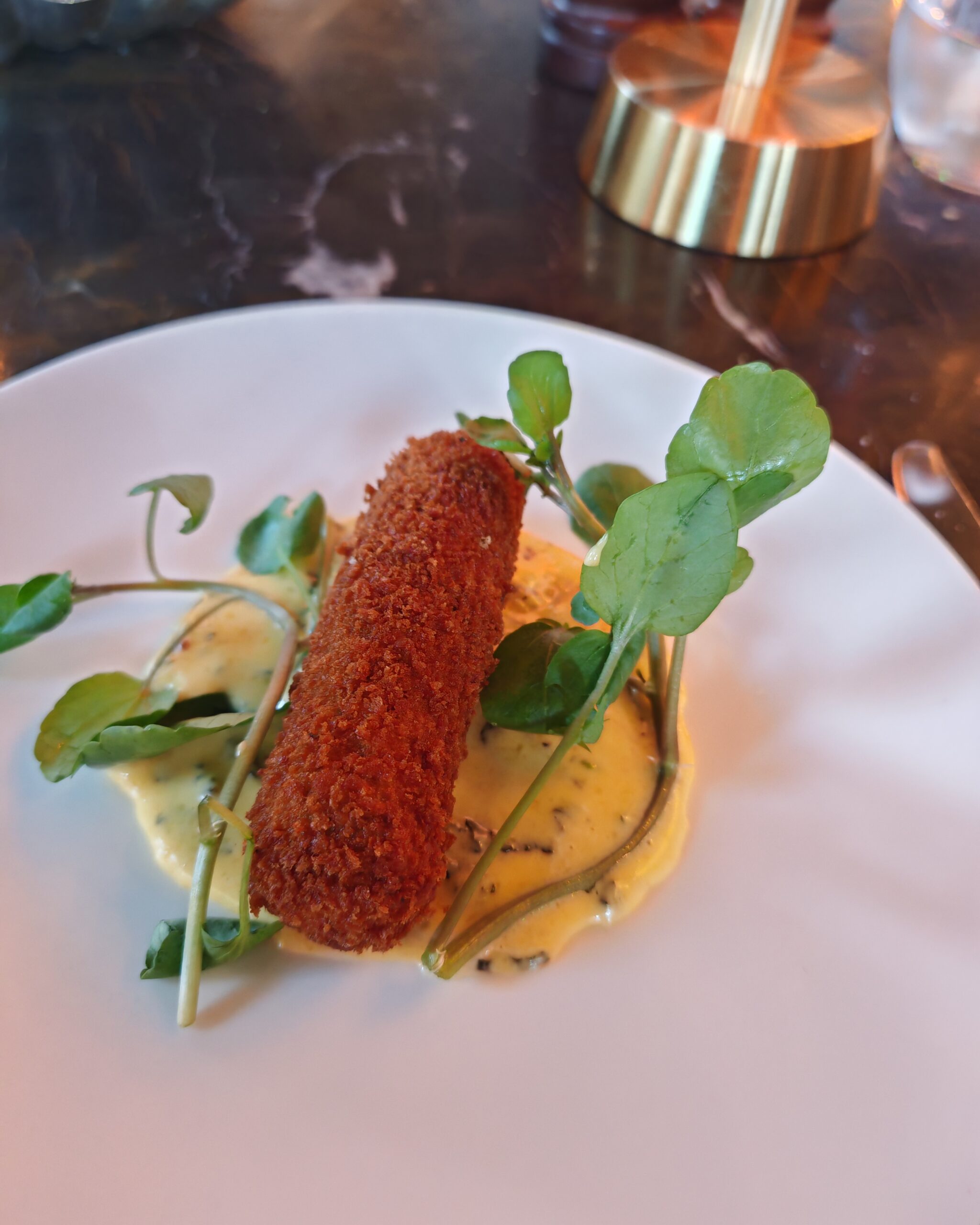 Lamb croquette cooked in a orange sauce and some parsley as a dressing in a white plate
