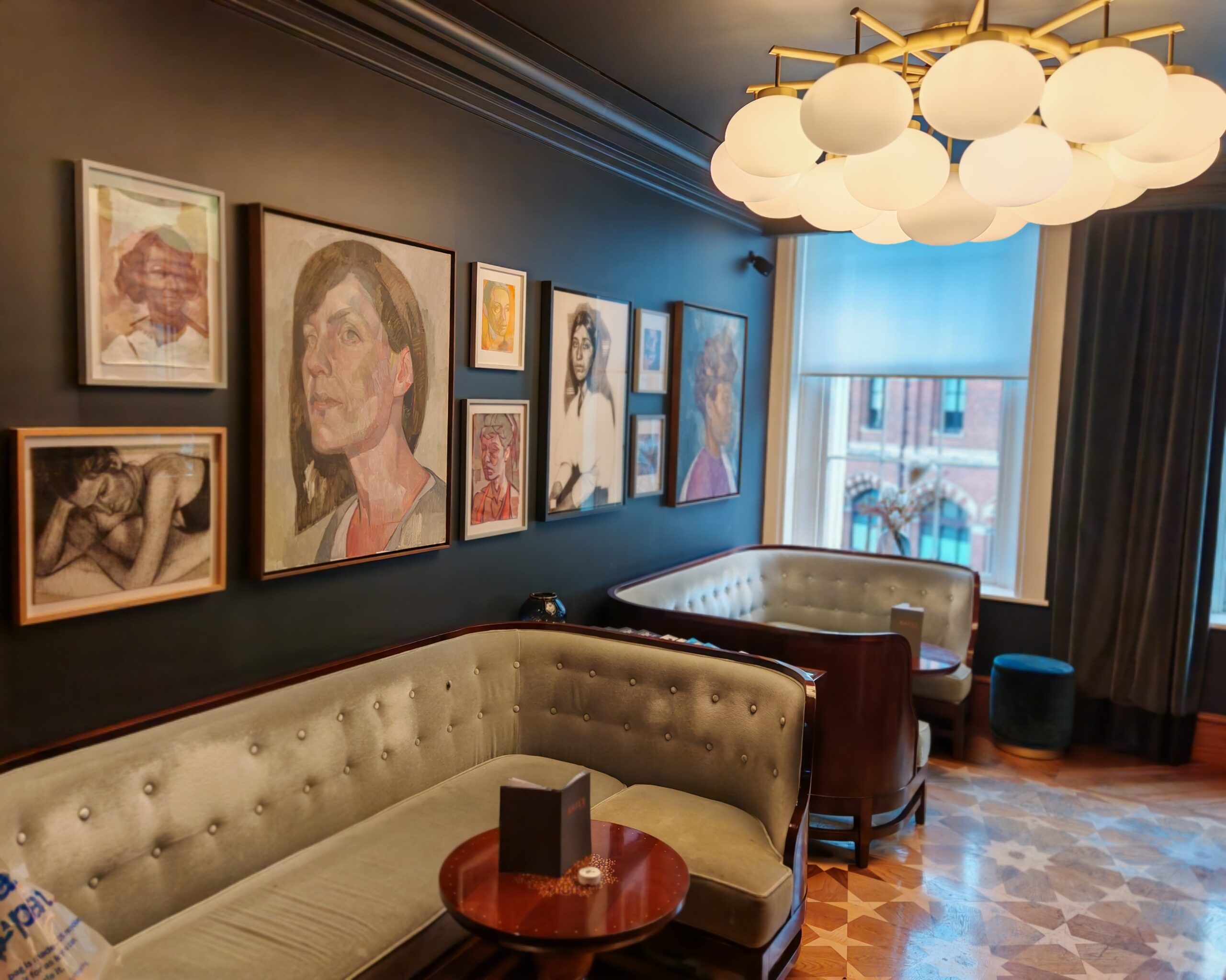 Interiors of the Little Bar at Rails Restaurant in Central London with modern lightings and two large beige velvet sofas below modern art portraits