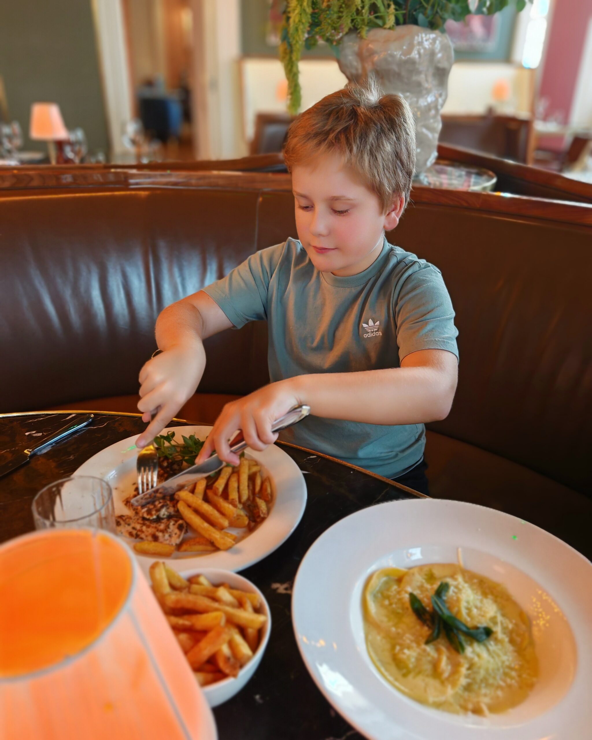 White little boy in a green adidas tee shirt eating chicken and fries at the Rails Restaurant opposite St Pancras station
