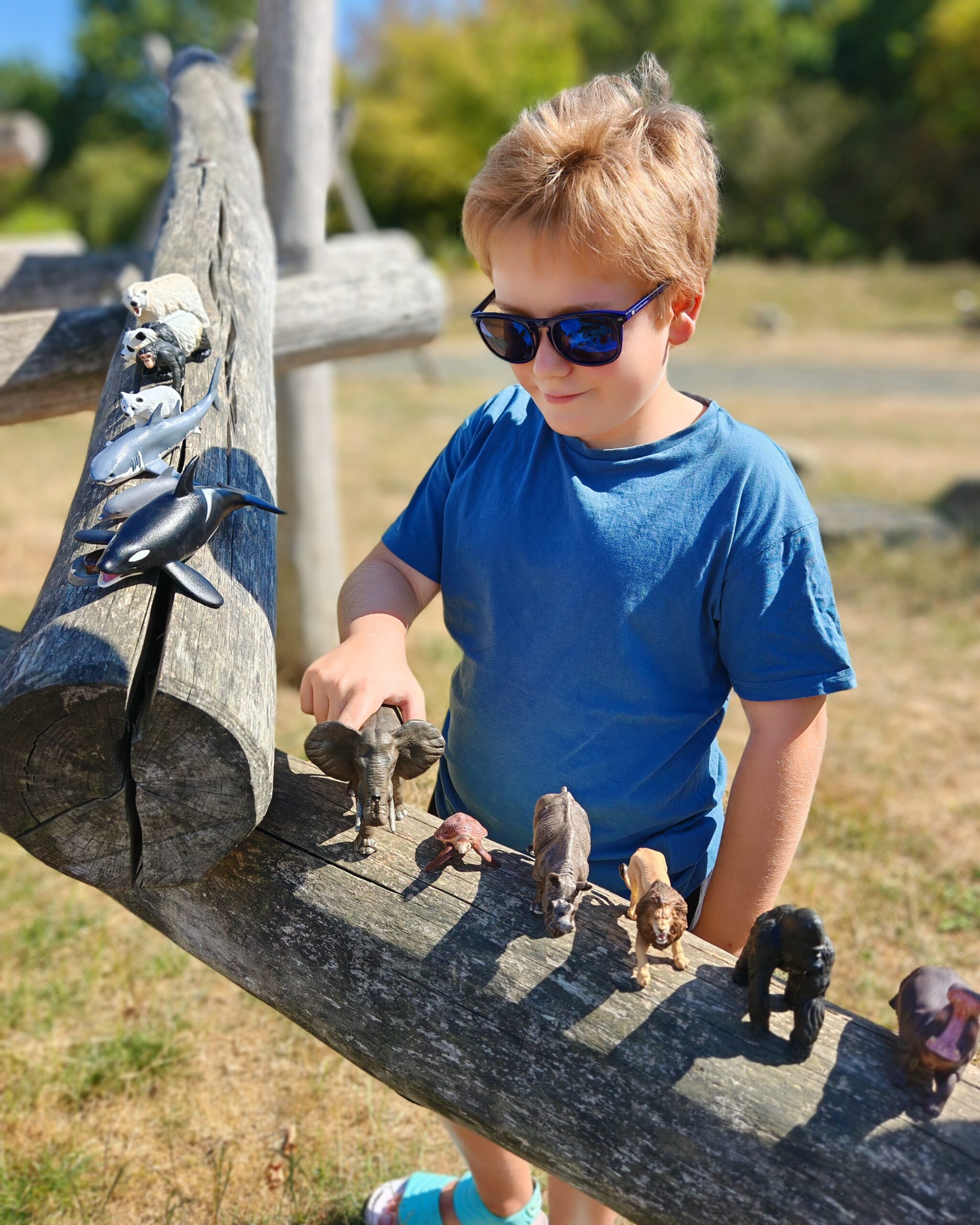 White little boy with blond hair playing with animal figurines in a park