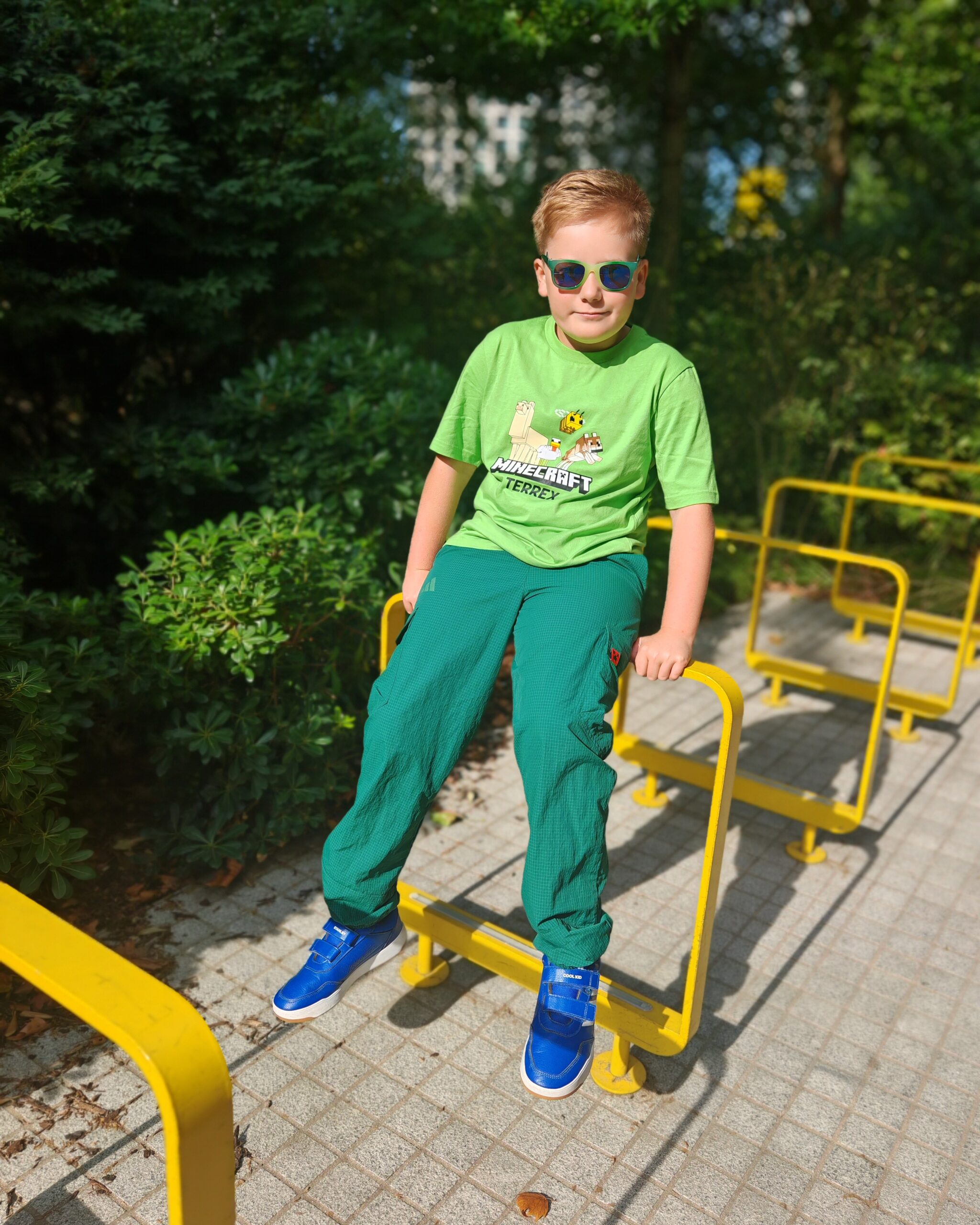 White little boy wearing a bright green tee from the latest adidas x Minecraft Collaboration sitting on a bike rack in Elephant & Castle