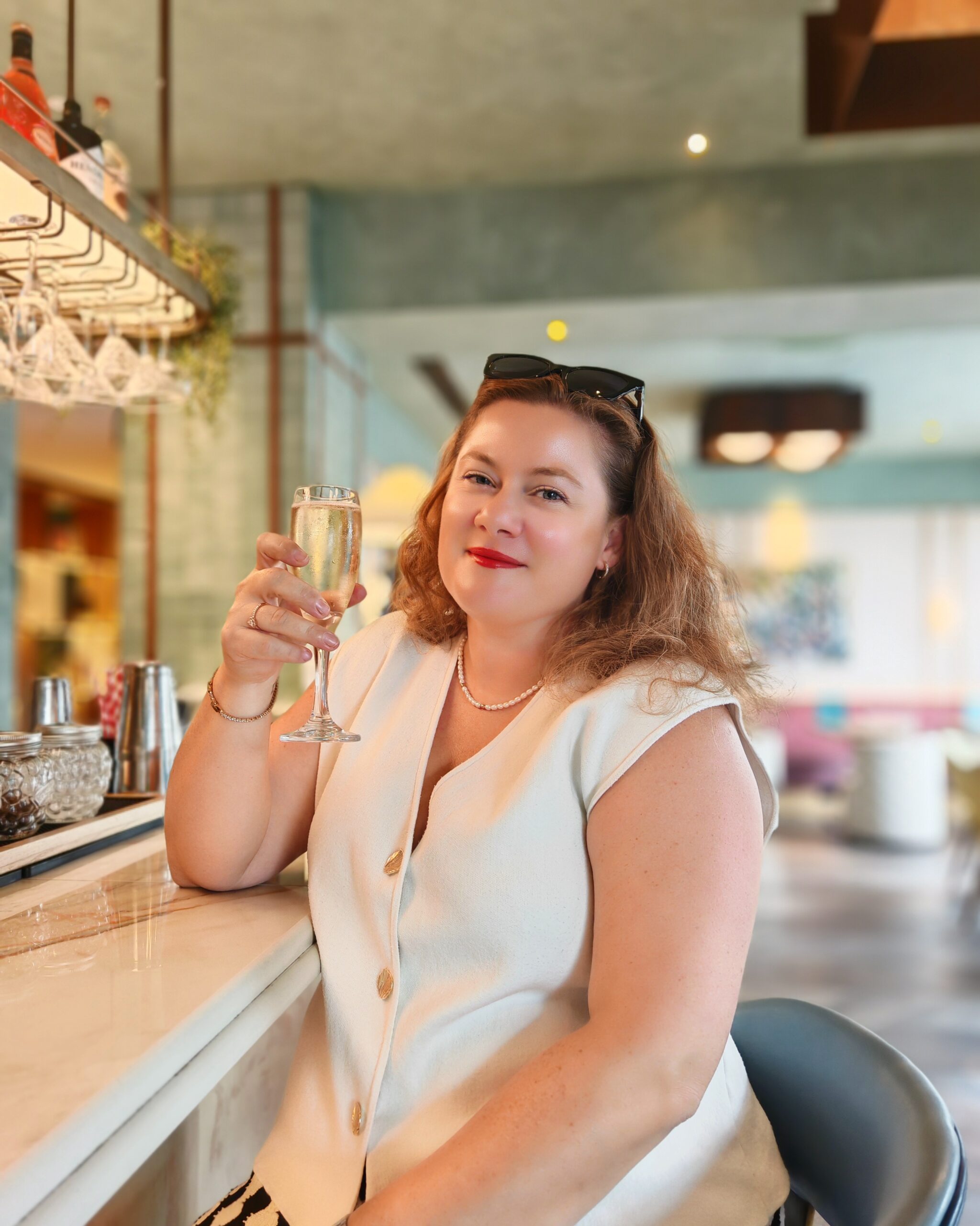 white woman with a white top holding a glass of prosecco at the bar of the Double Tree Hotel by Hilton in London Victoria