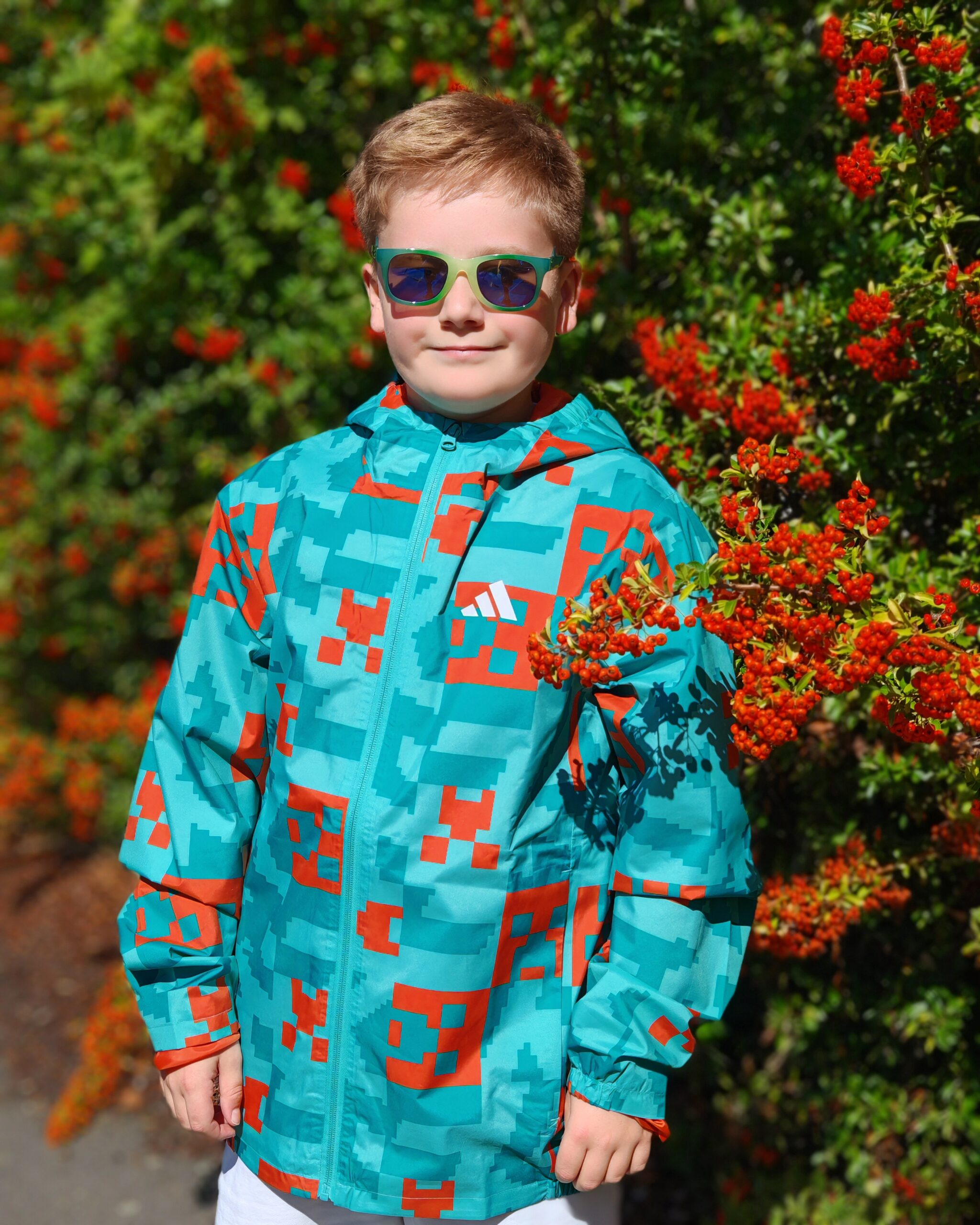 White little boy wearing a bright blue and orange rain jacket from the latest adidas x Minecraft Collaboration. It's the adidas x Minecraft Terrex 2 Layer Rain Jacket design