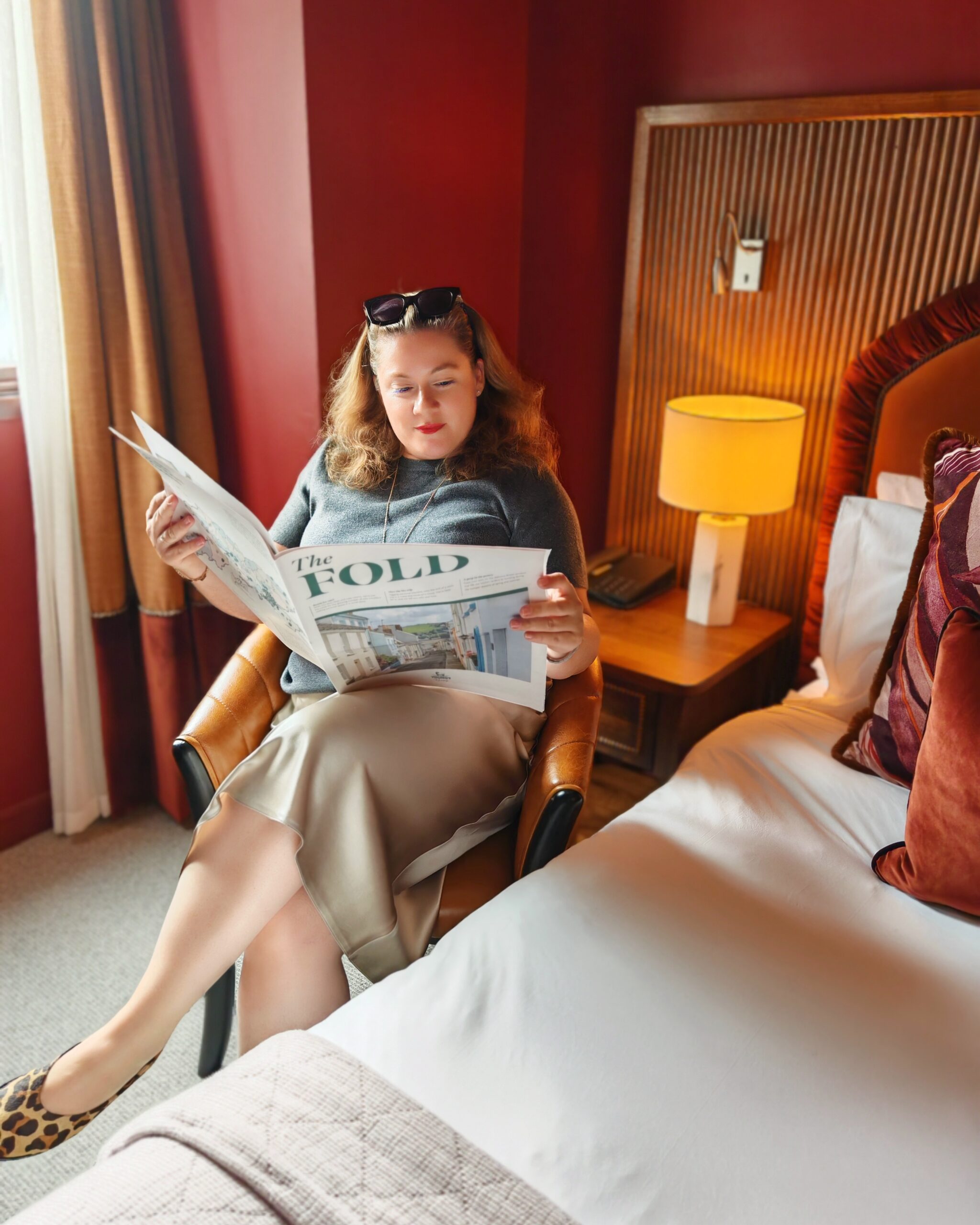 white woman in a charcoal grey sweater and beige silk skirt, reading the Fold newspaper in her room at the young's pub the Chertsey in Surrey white woman in a charcoal grey sweater and beige silk skirt, reading the Fold newspaper in her room at the young's pub the Chertsey in Surrey