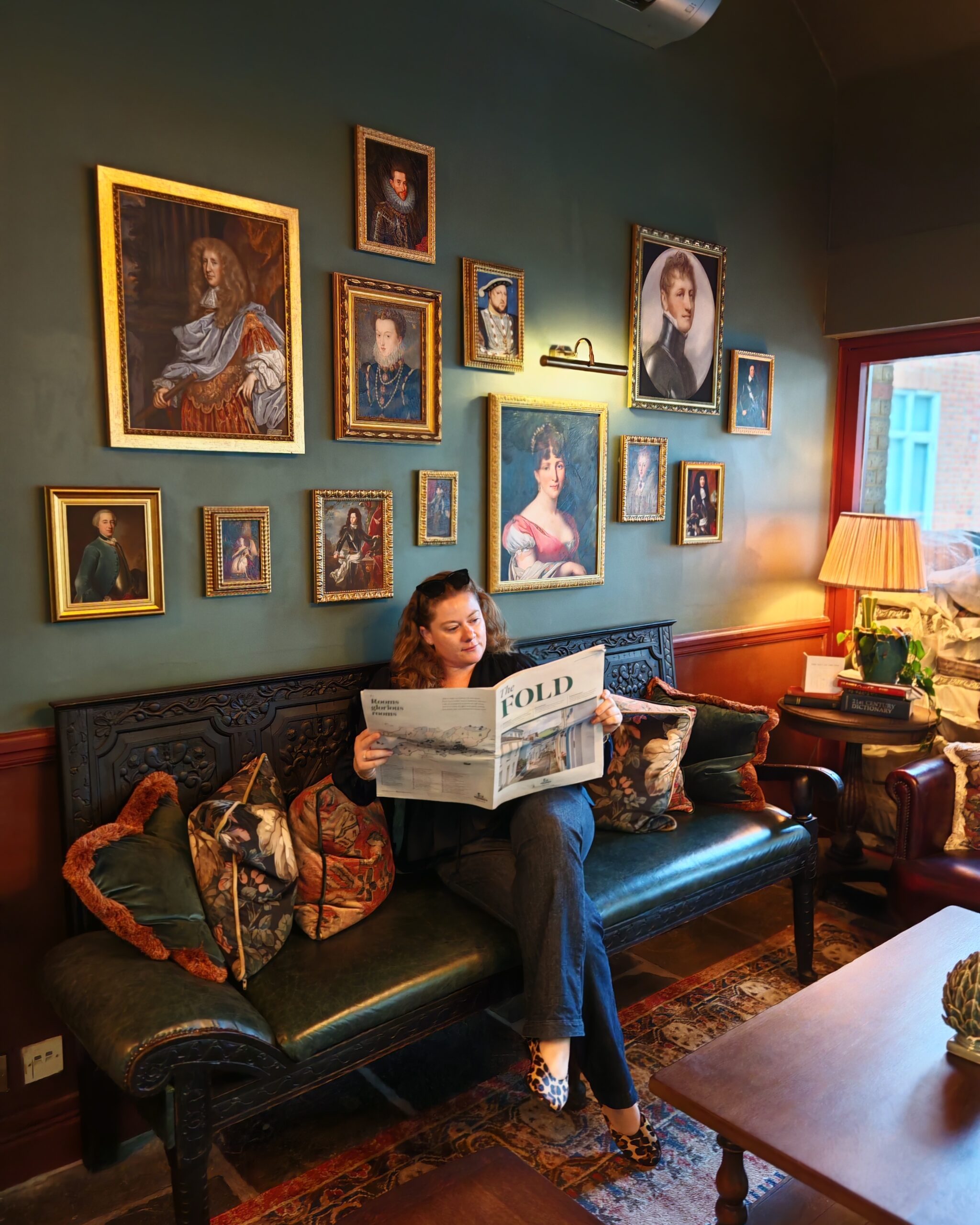white woman in a blue sating top and jeans, sitting at the reception of the Crown hotel in Chertsey. She's surrounded by old paintings while reading a copy of the Fold newspaper white woman in a blue sating top and jeans, sitting at the reception of the Crown hotel in Chertsey. She's surrounded by old paintings while reading a copy of the Fold newspaper