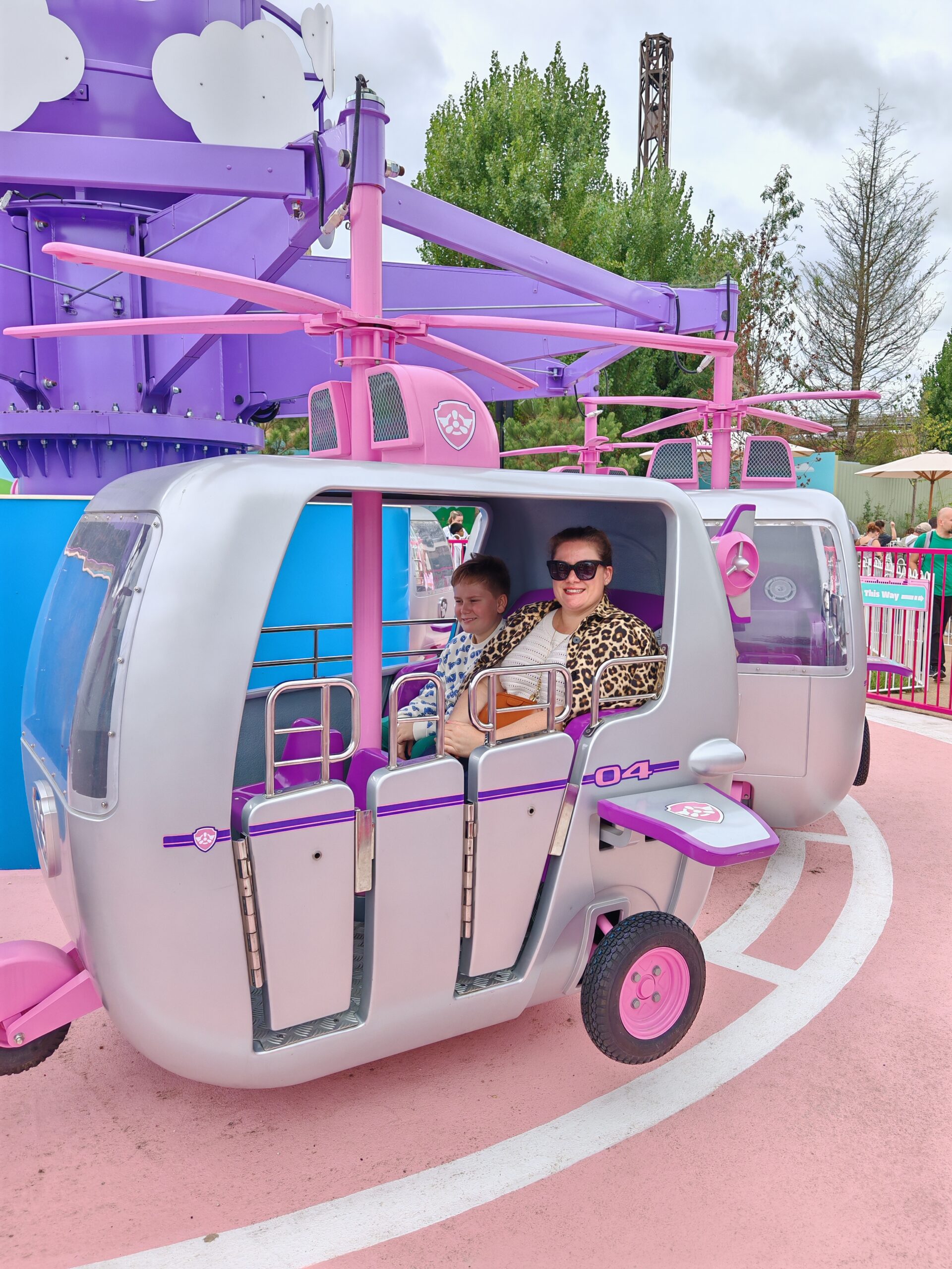 White woman in a leopard jacket and her son on the Sky ride, which is made of purple helicopters with pink wheels White woman in a leopard jacket and her son on the Sky ride, which is made of purple helicopters with pink wheels