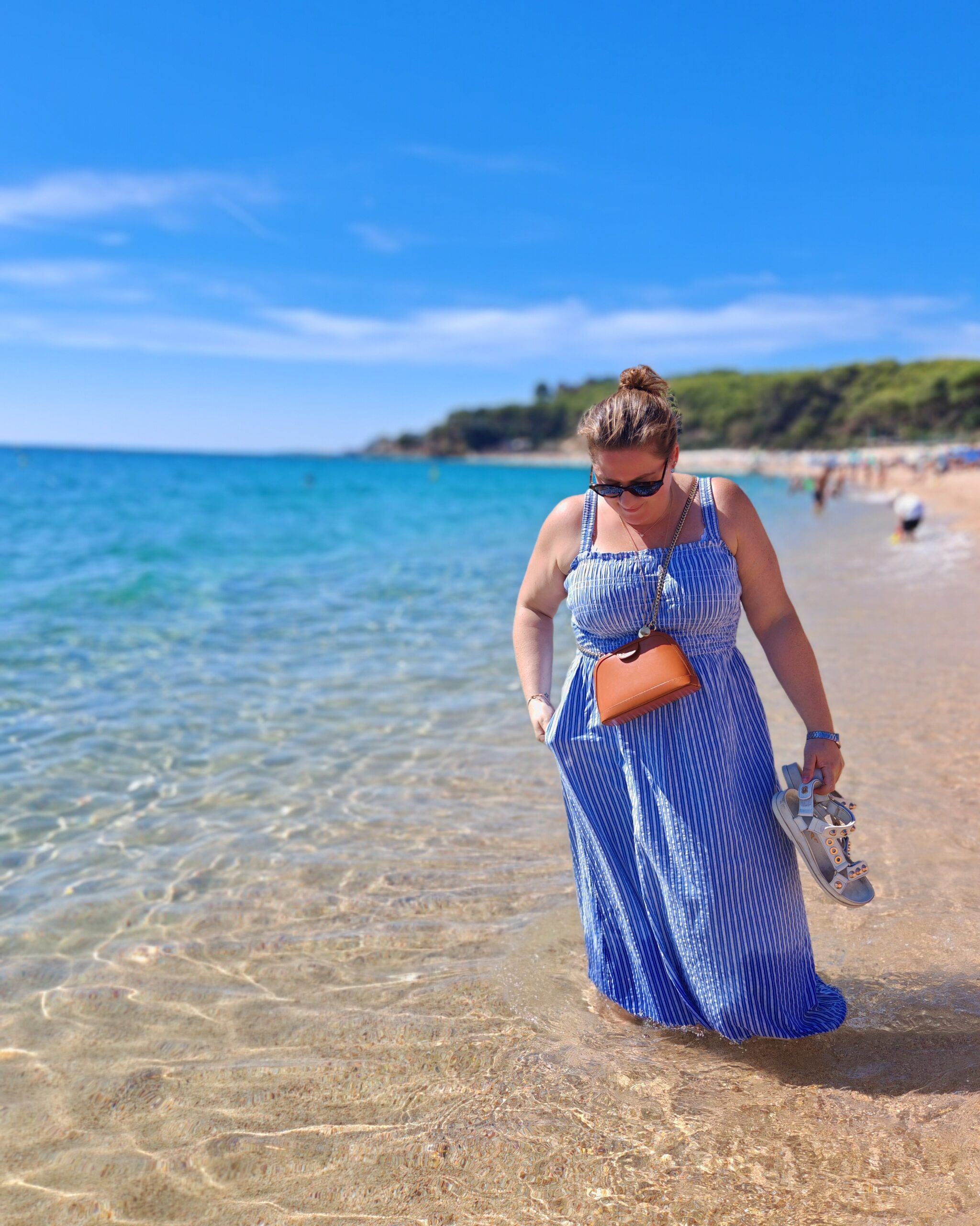 white woman in a long blue summer dress, her feet in the water by the beach in Lloret de Mar white woman in a long blue summer dress, her feet in the water by the beach in Lloret de Mar