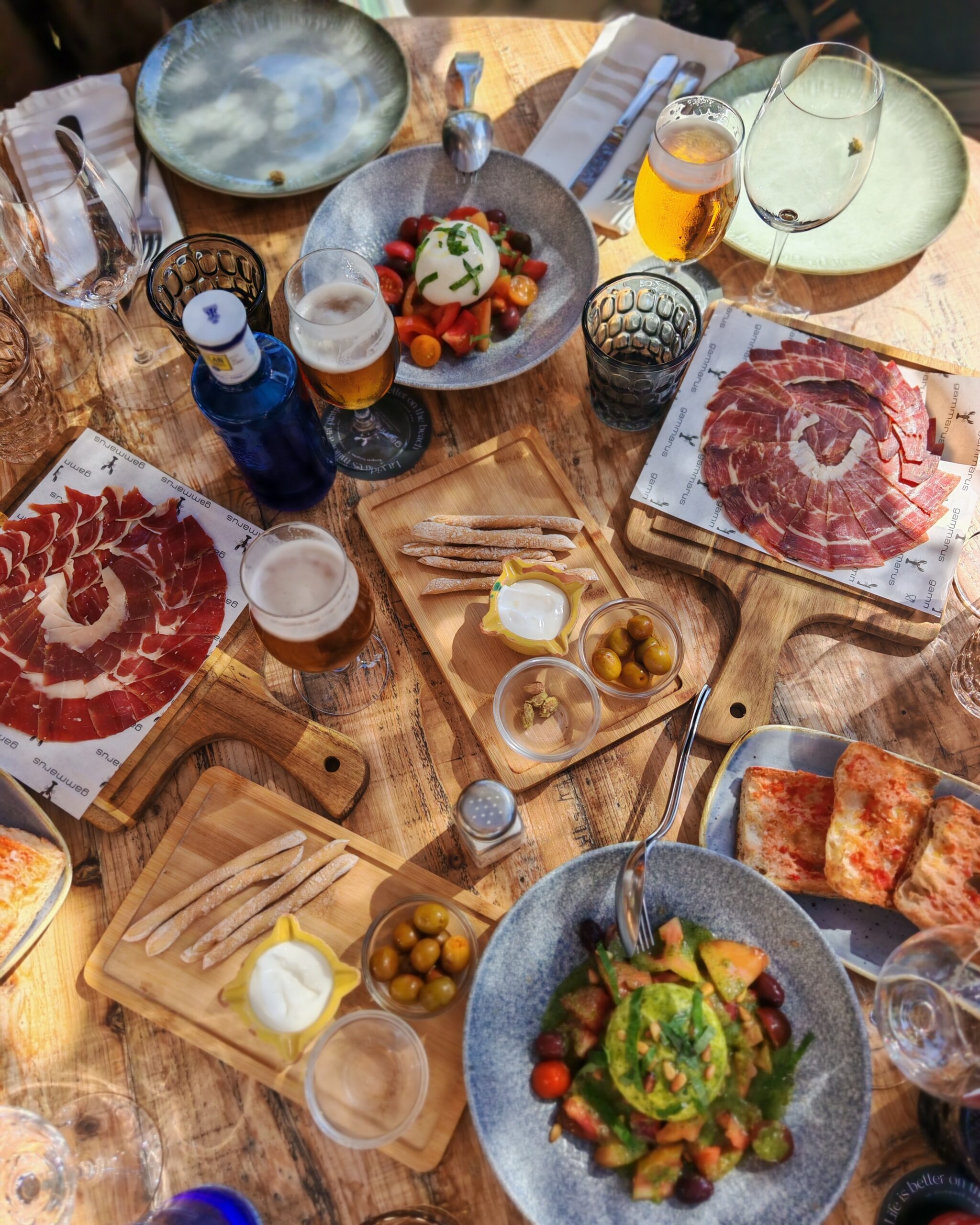 Flat lay of food at Gammarus Restaurant & Beach Club with burrata, ham, pan con tomate and a selection of drinks in the sunshine Flat lay of food at Gammarus Restaurant & Beach Club with burrata, ham, pan con tomate and a selection of drinks in the sunshine