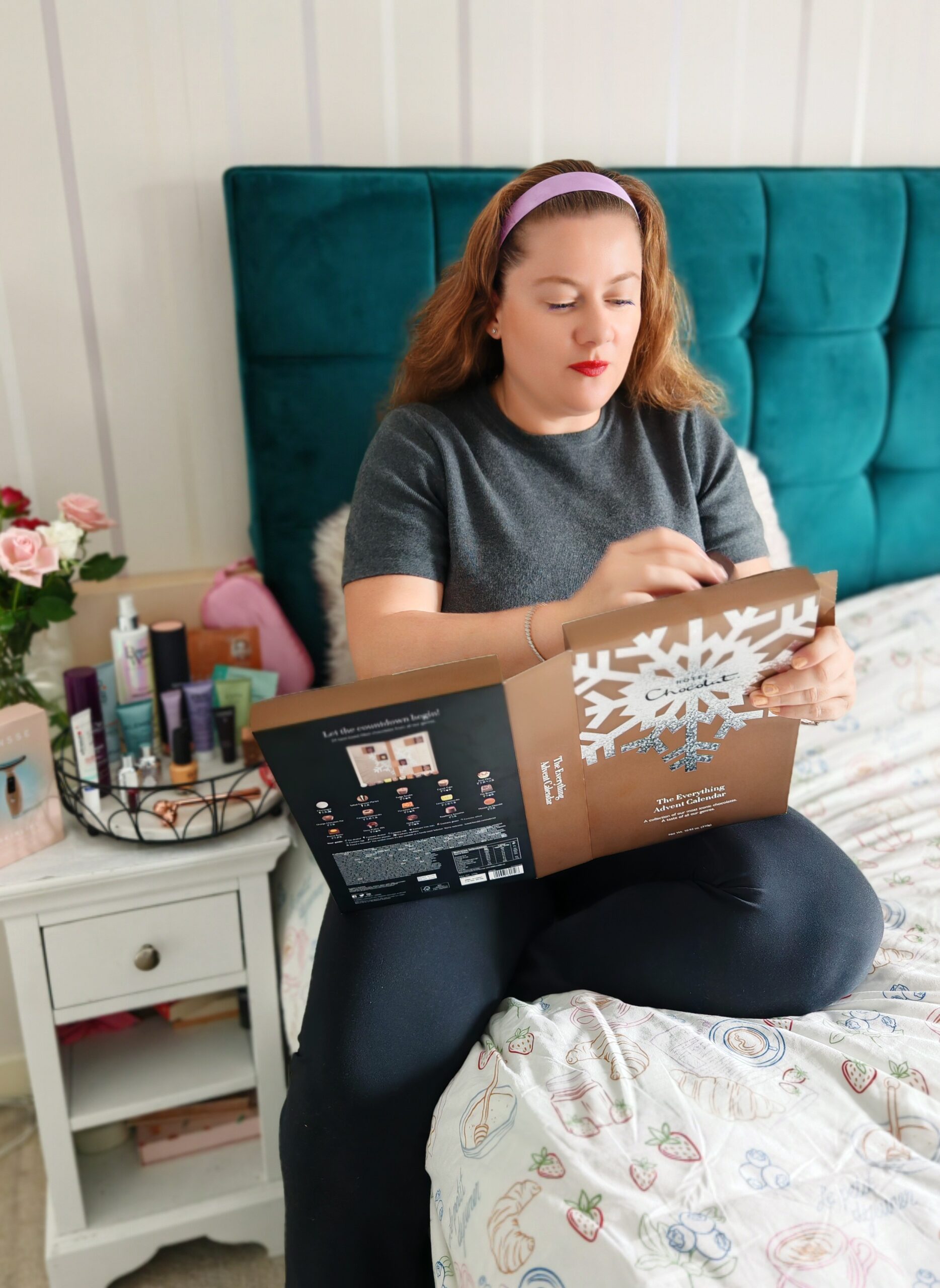 White woman on her bed with black trousers and a dark grey jumper, opening an hotel chocolat advent calendar White woman on her bed with black trousers and a dark grey jumper, opening an hotel chocolat advent calendar